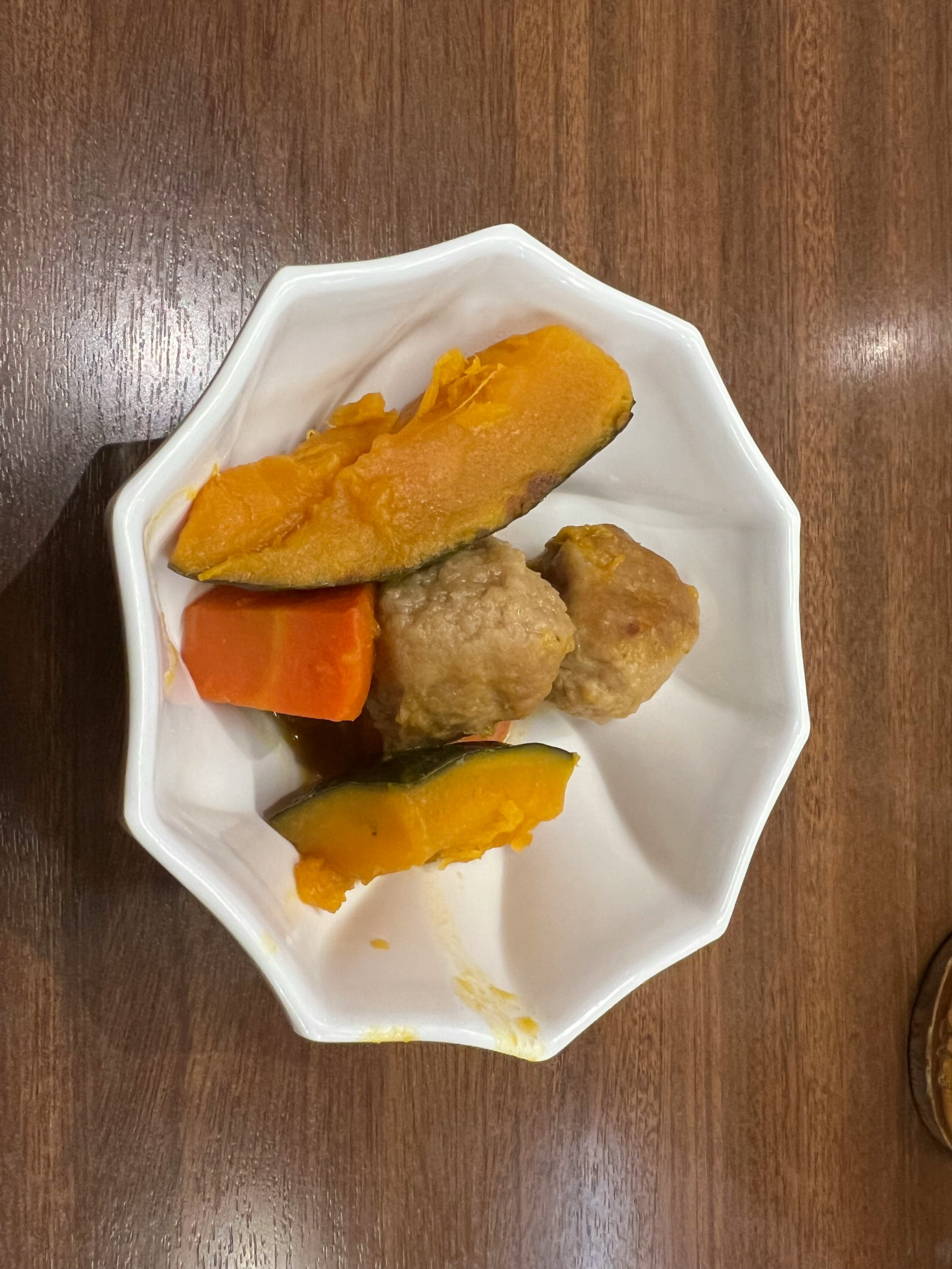 A white dish containing pumpkin, carrot, and meatballs