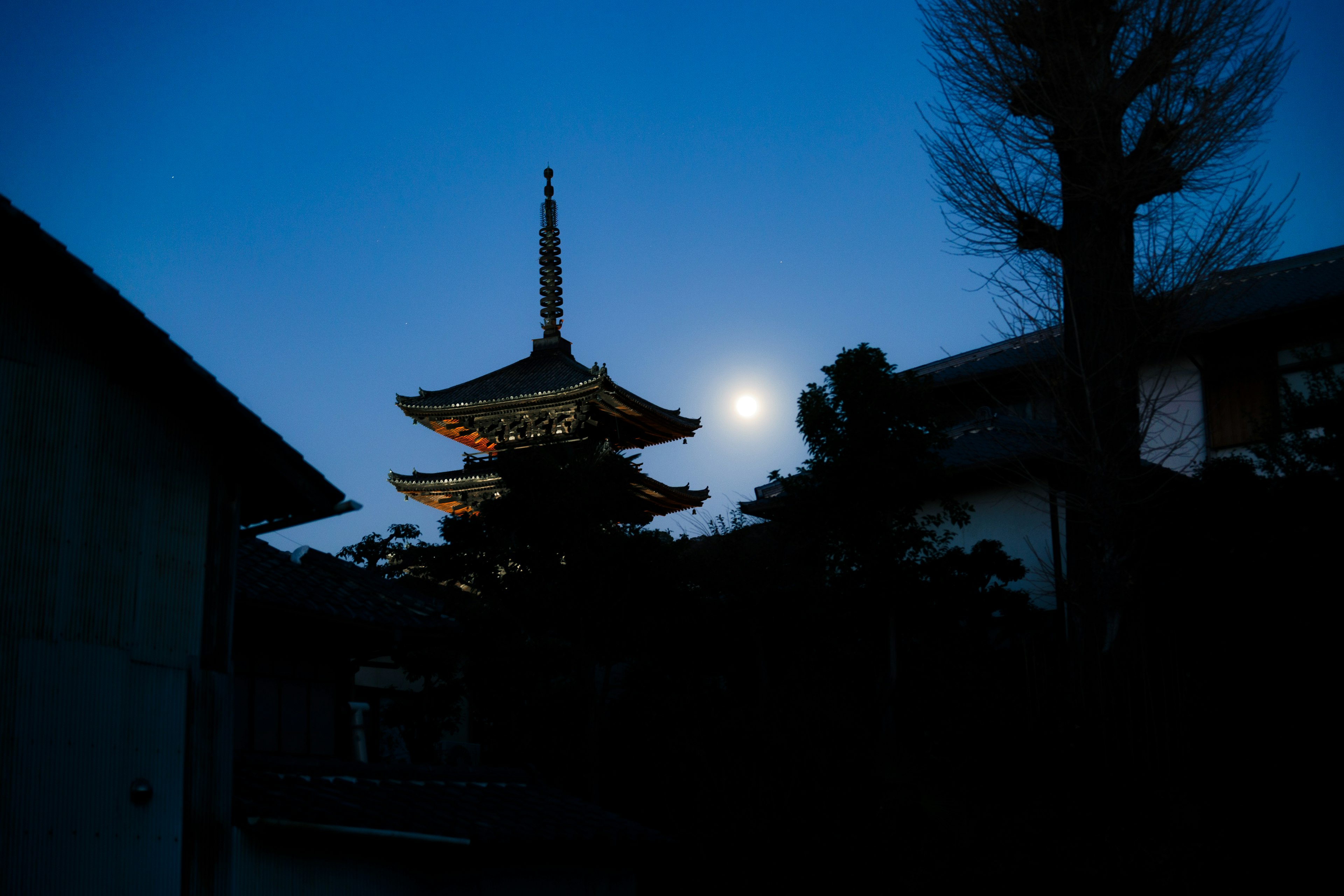 Silhouette of a pagoda against the night sky with a full moon