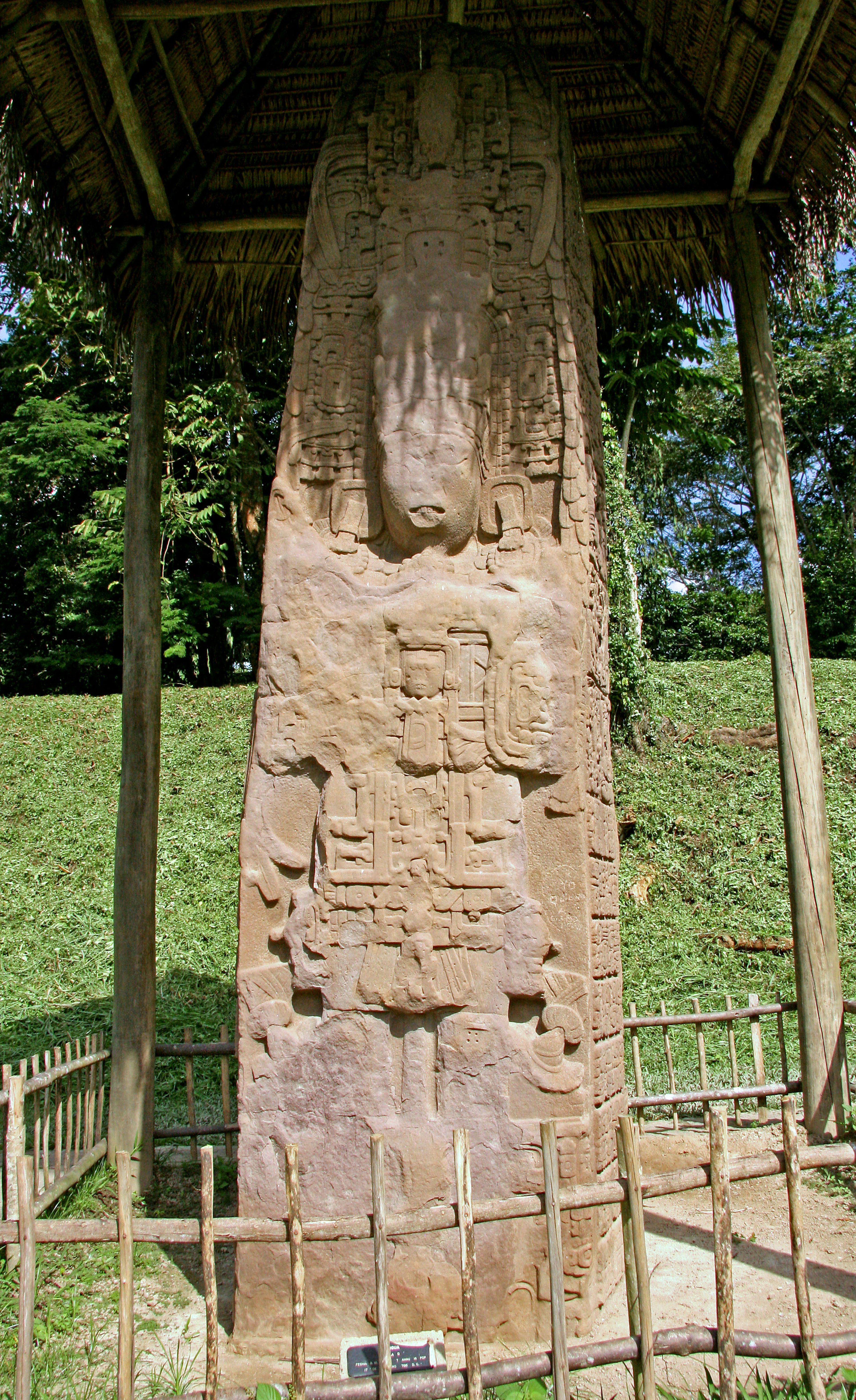 Altes Steindenkmal in einem Strohdachunterstand mit grünem Gras umgeben