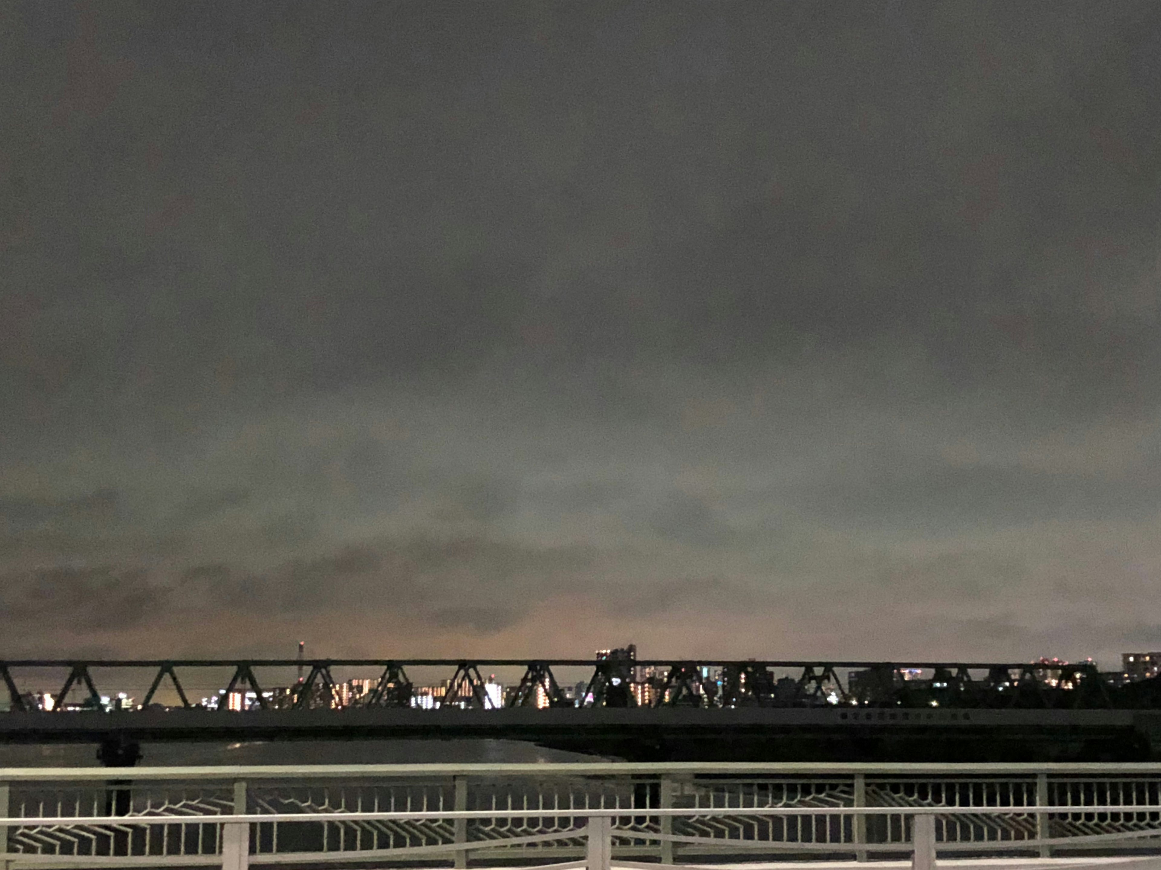 Jembatan di bawah langit gelap dengan lampu kota di kejauhan