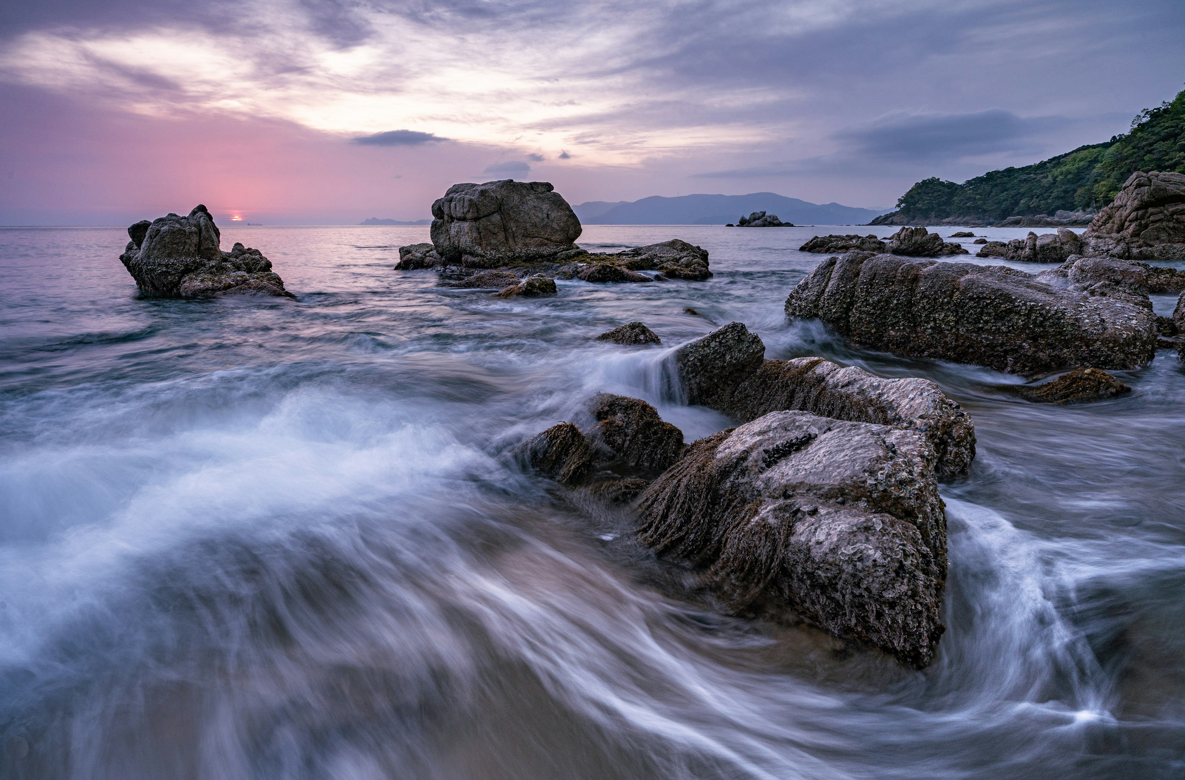 Sunset over the ocean with rocky shoreline and gentle waves