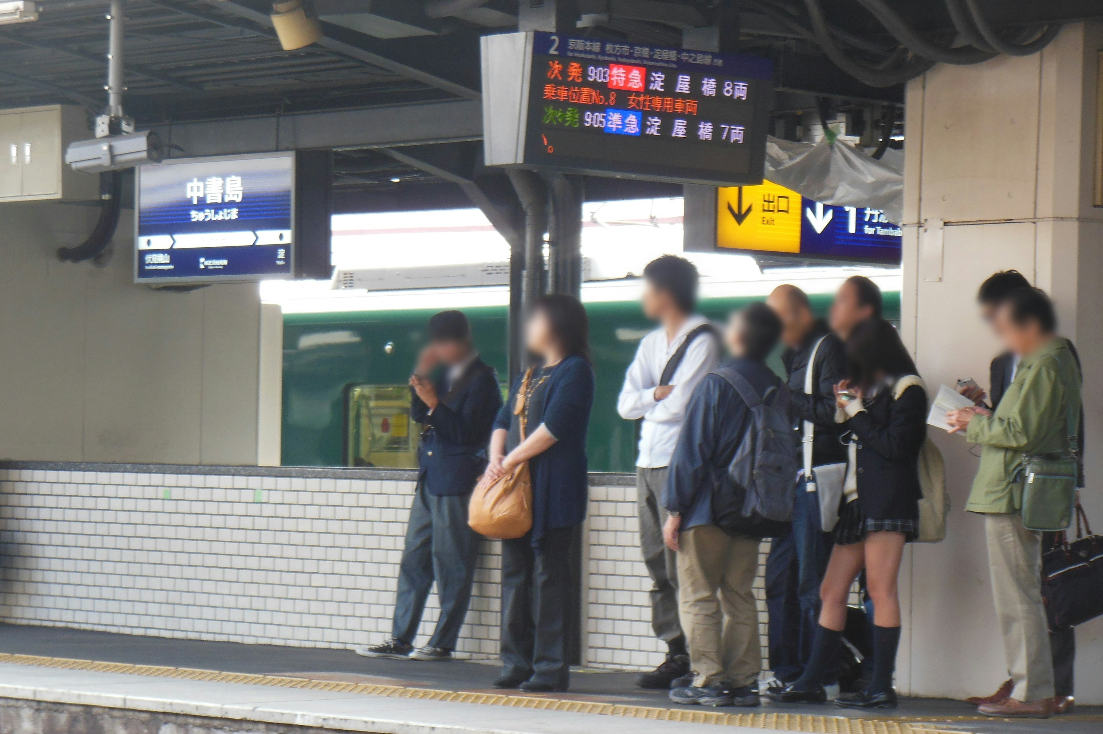 Menschen stehen auf einem Bahnsteig mit digitaler Anzeige