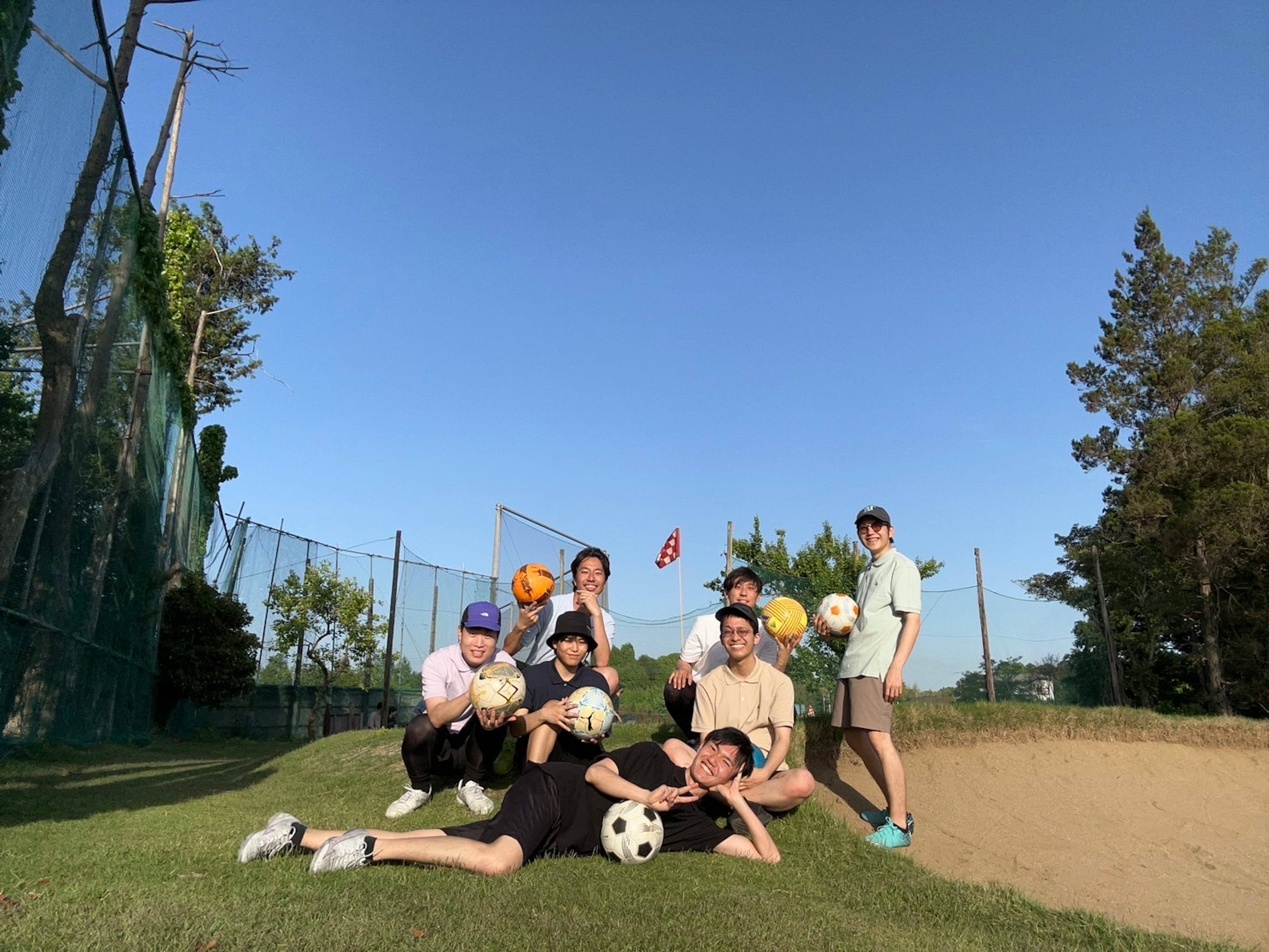 A group of young people posing with soccer balls under a clear blue sky