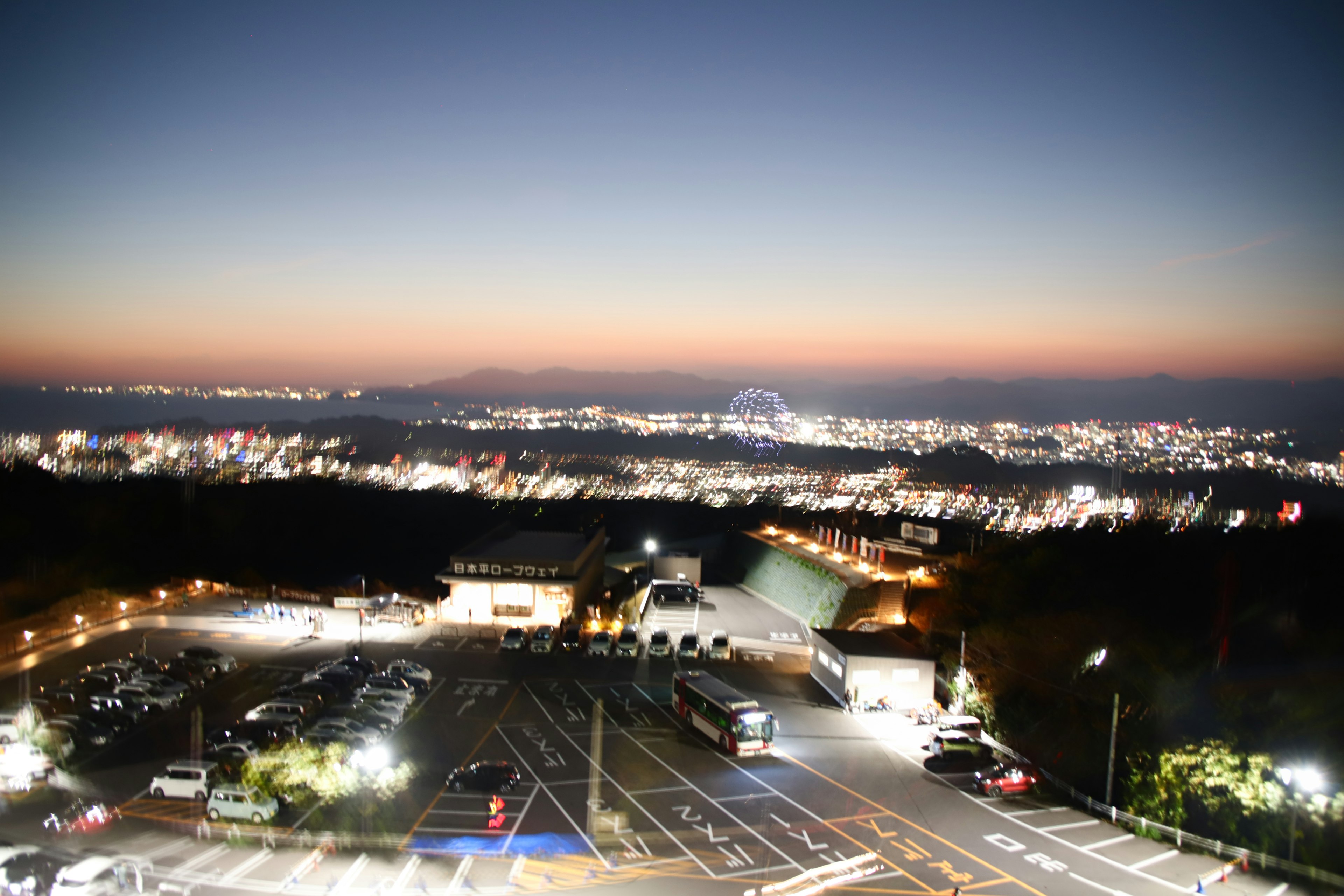 Vue nocturne d'un point élevé montrant un parking et des lumières de la ville