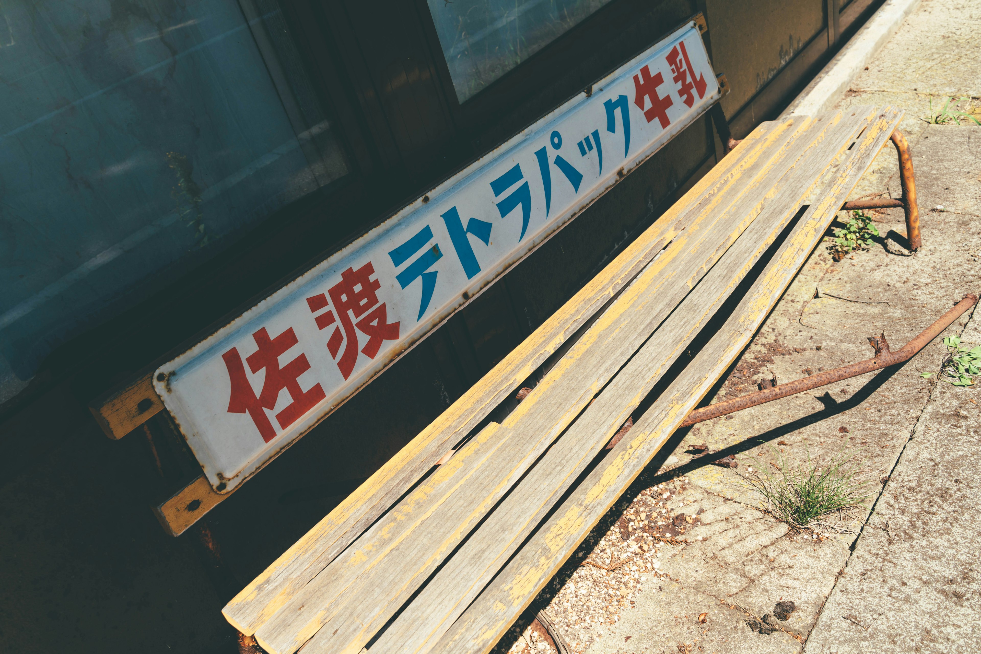 A weathered bench with a Japanese sign in a rural setting