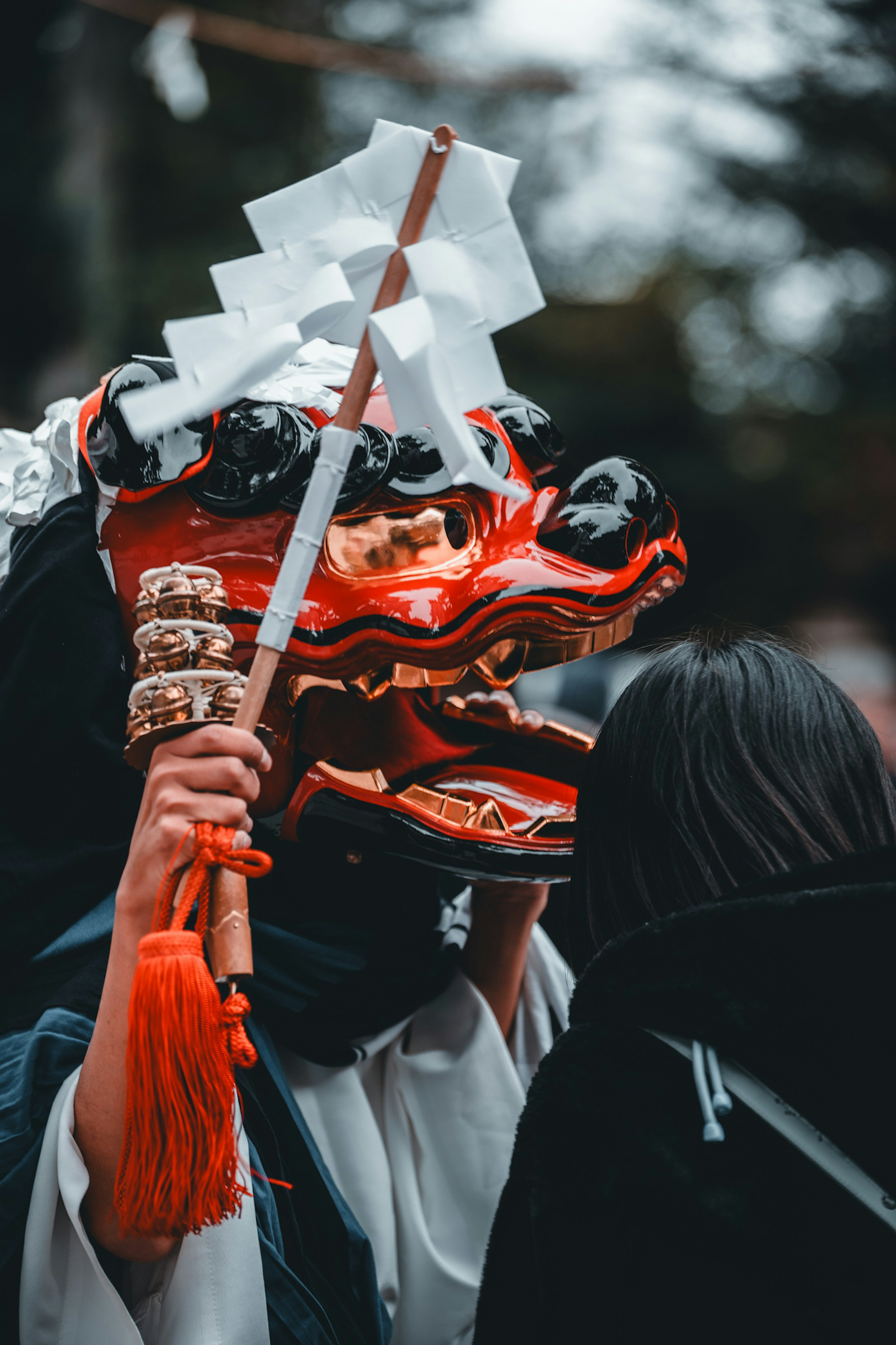 Person wearing a red lion dance mask holding a stick at a shrine