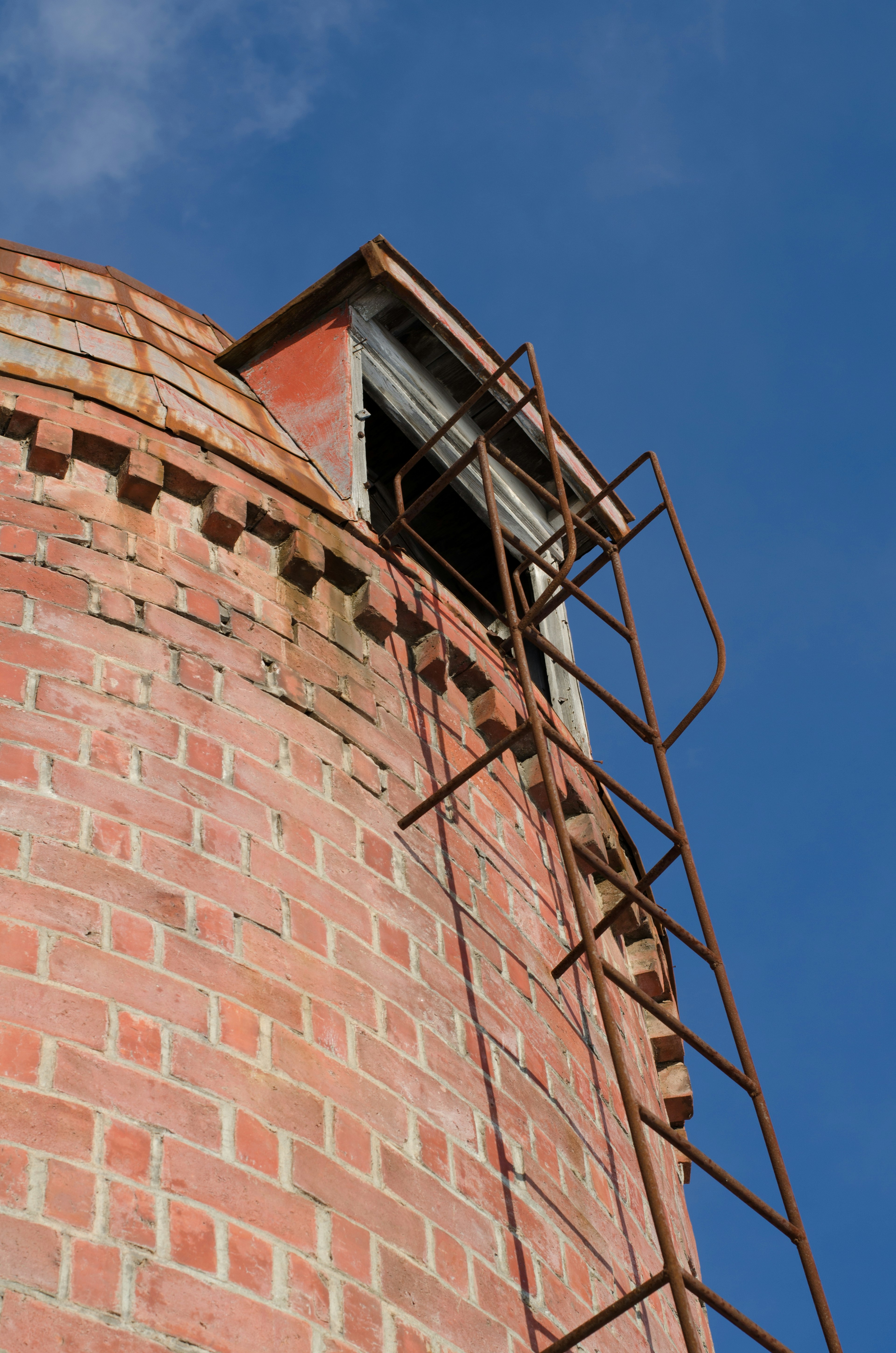 Silo de ladrillo antiguo con una escalera oxidada que lleva a la cima contra un cielo azul