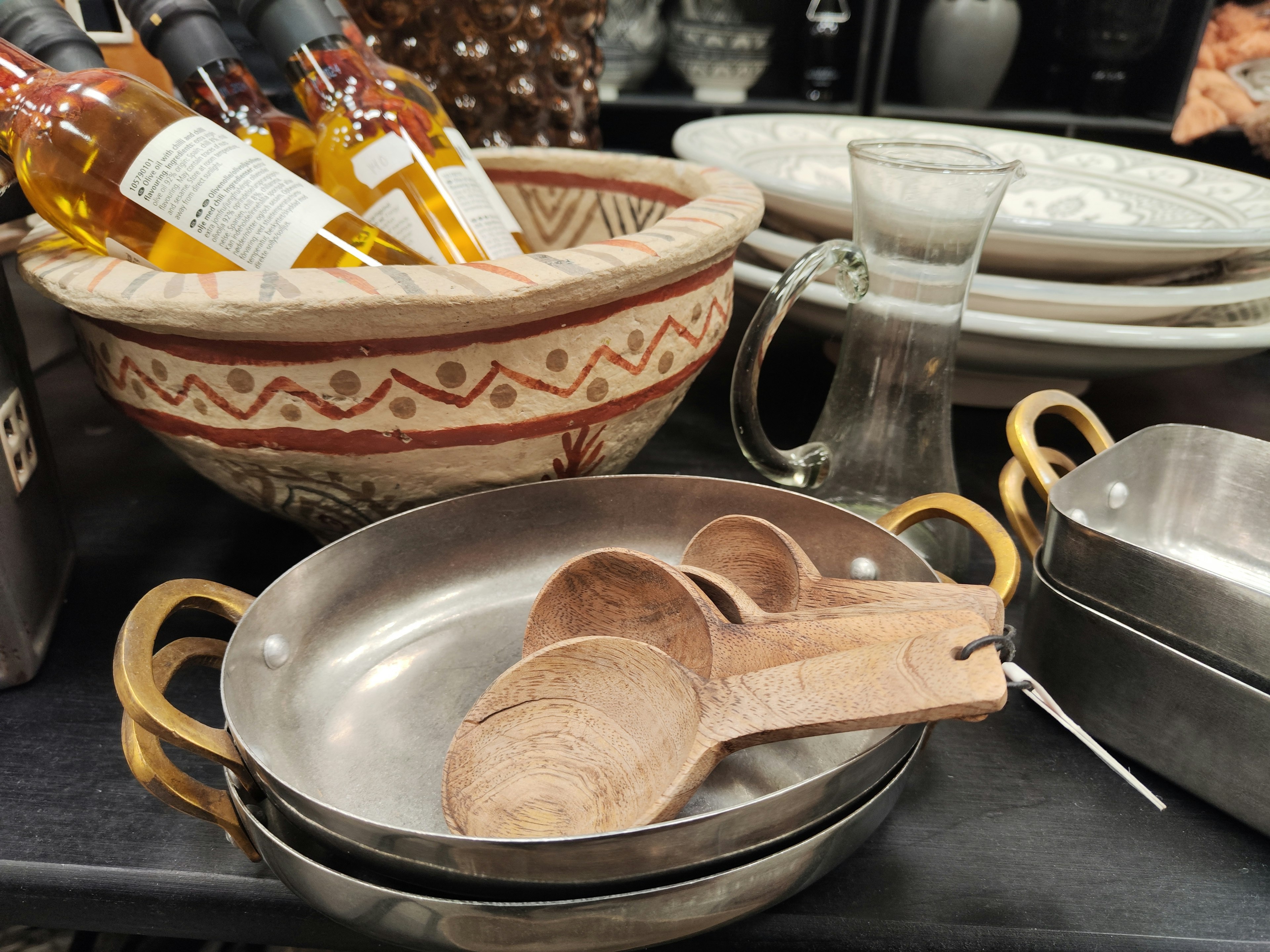 Wooden spoons and metal bowls arranged with wine bottles and a ceramic bowl on a table