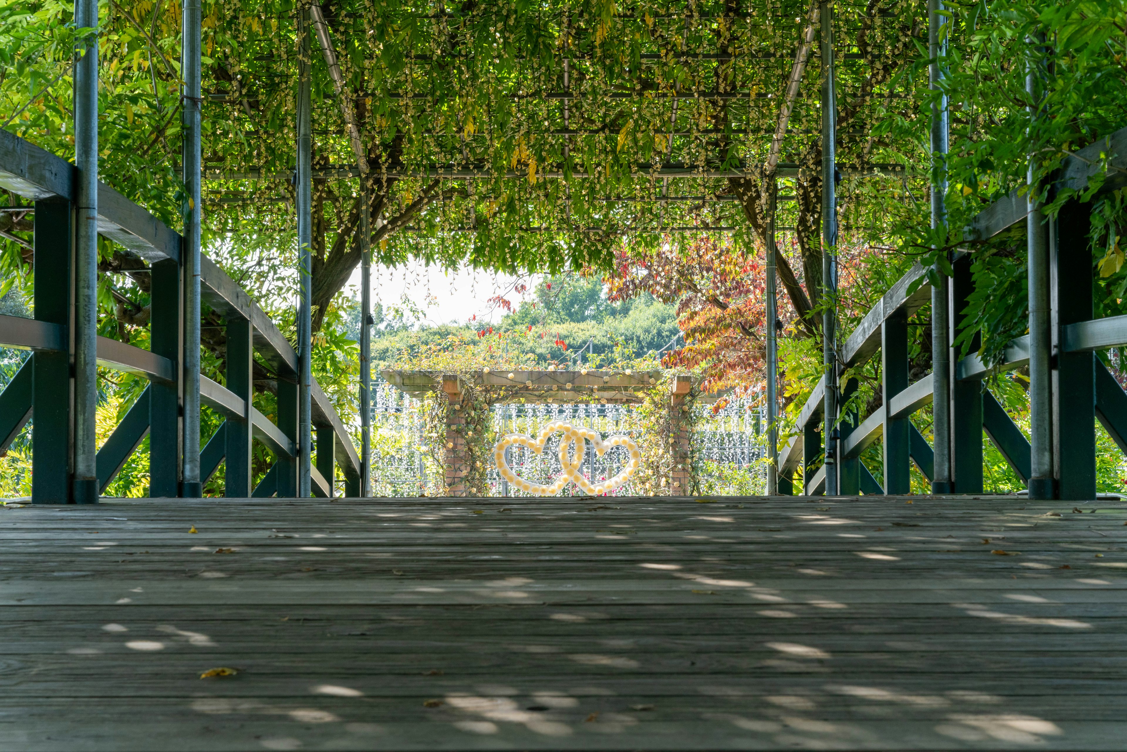 Vista di un ponte in legno che conduce a un arco verde con la luce del sole che filtra