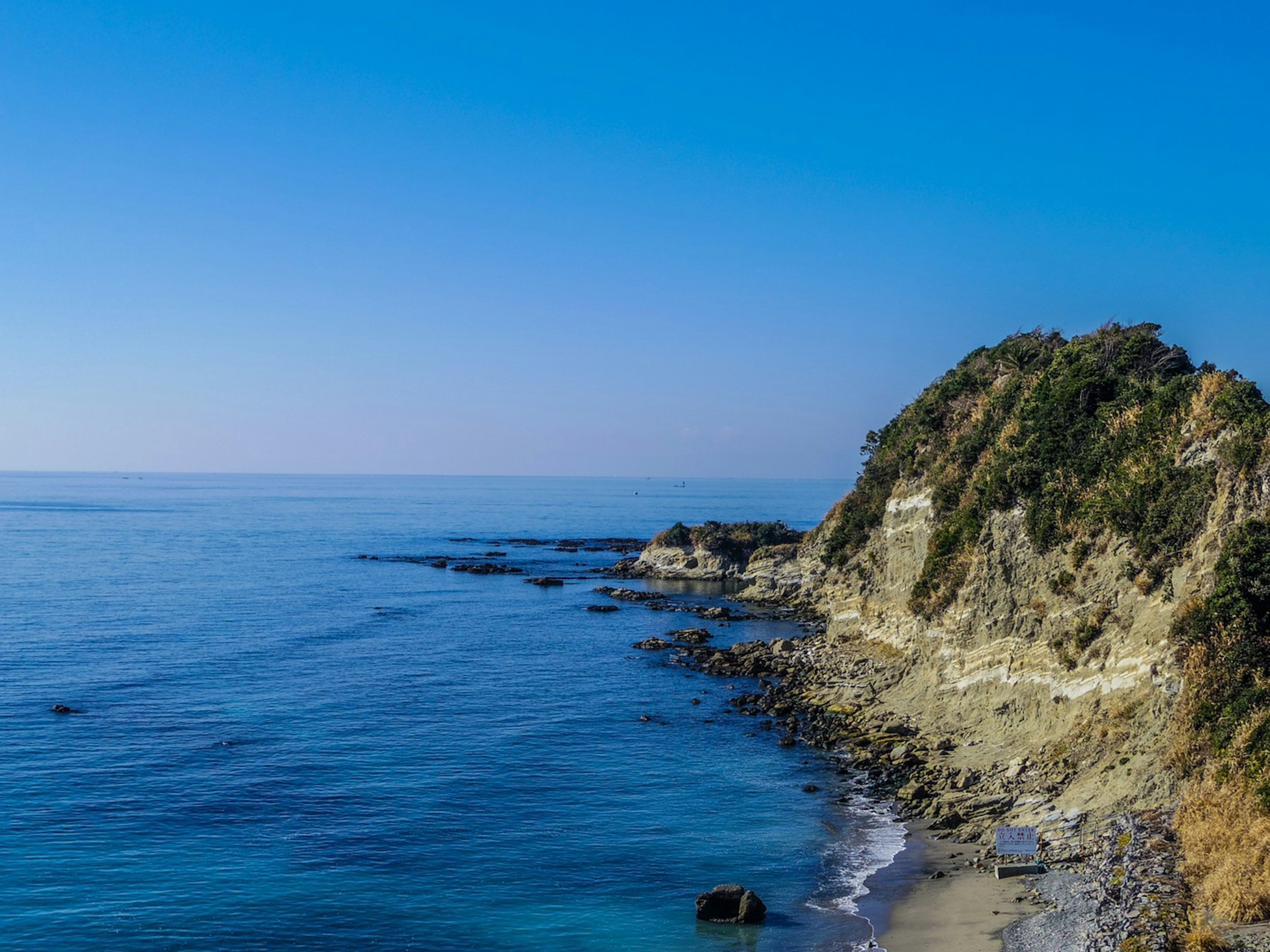 Scenic view of calm ocean under a blue sky featuring a rocky cliff and sandy beach