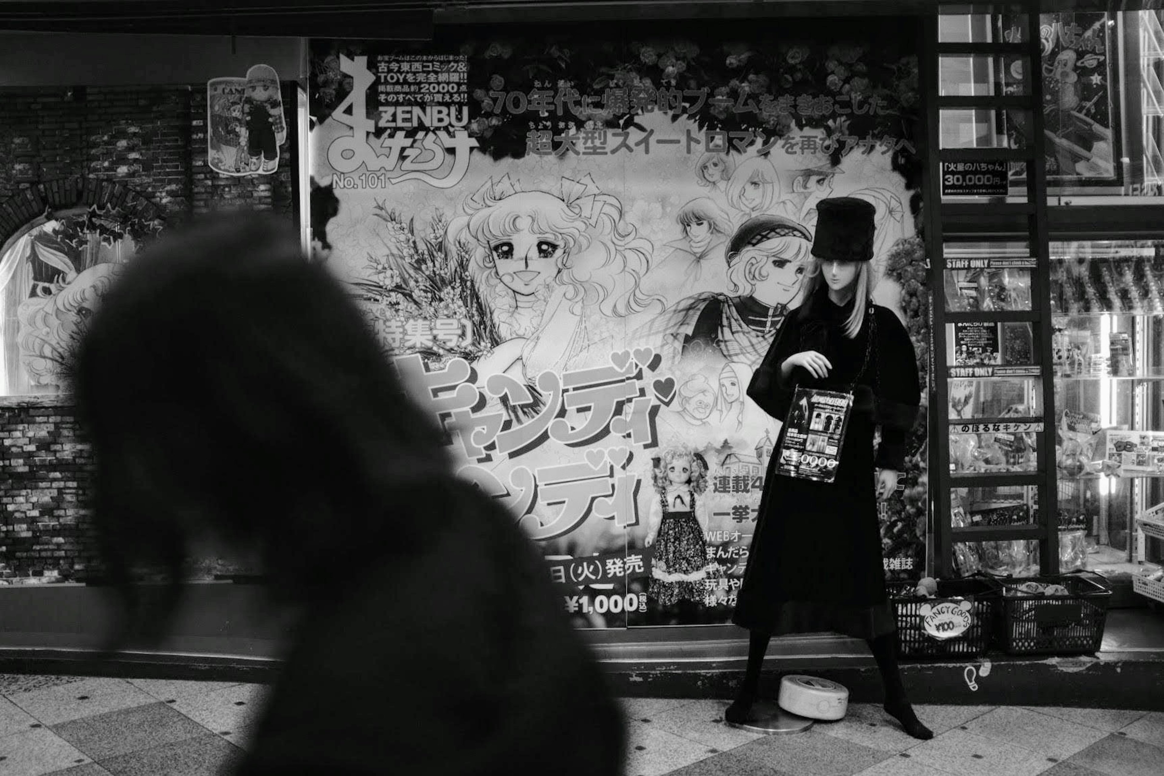 Escena de calle en blanco y negro con una persona en abrigo negro frente a un graffiti colorido