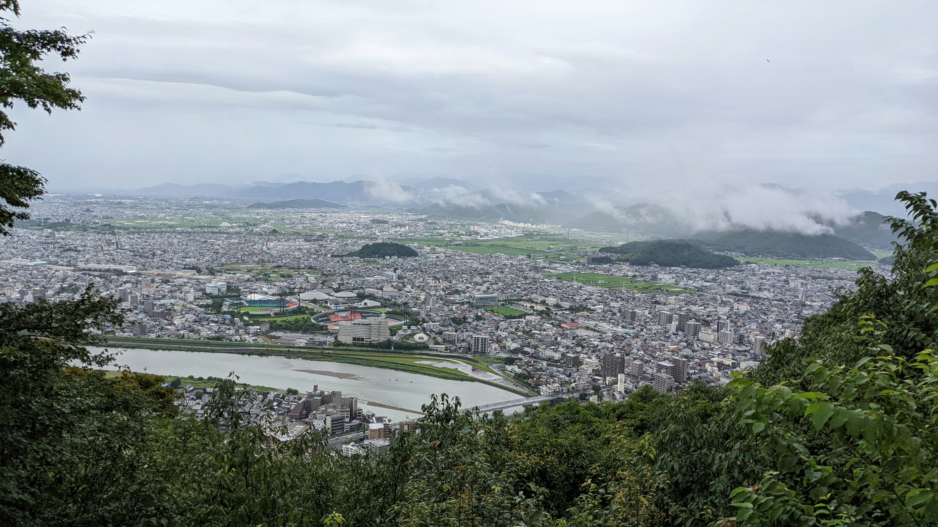 Panoramablick auf eine Stadt von einem Berggipfel mit bewölktem Himmel und üppigem Grün