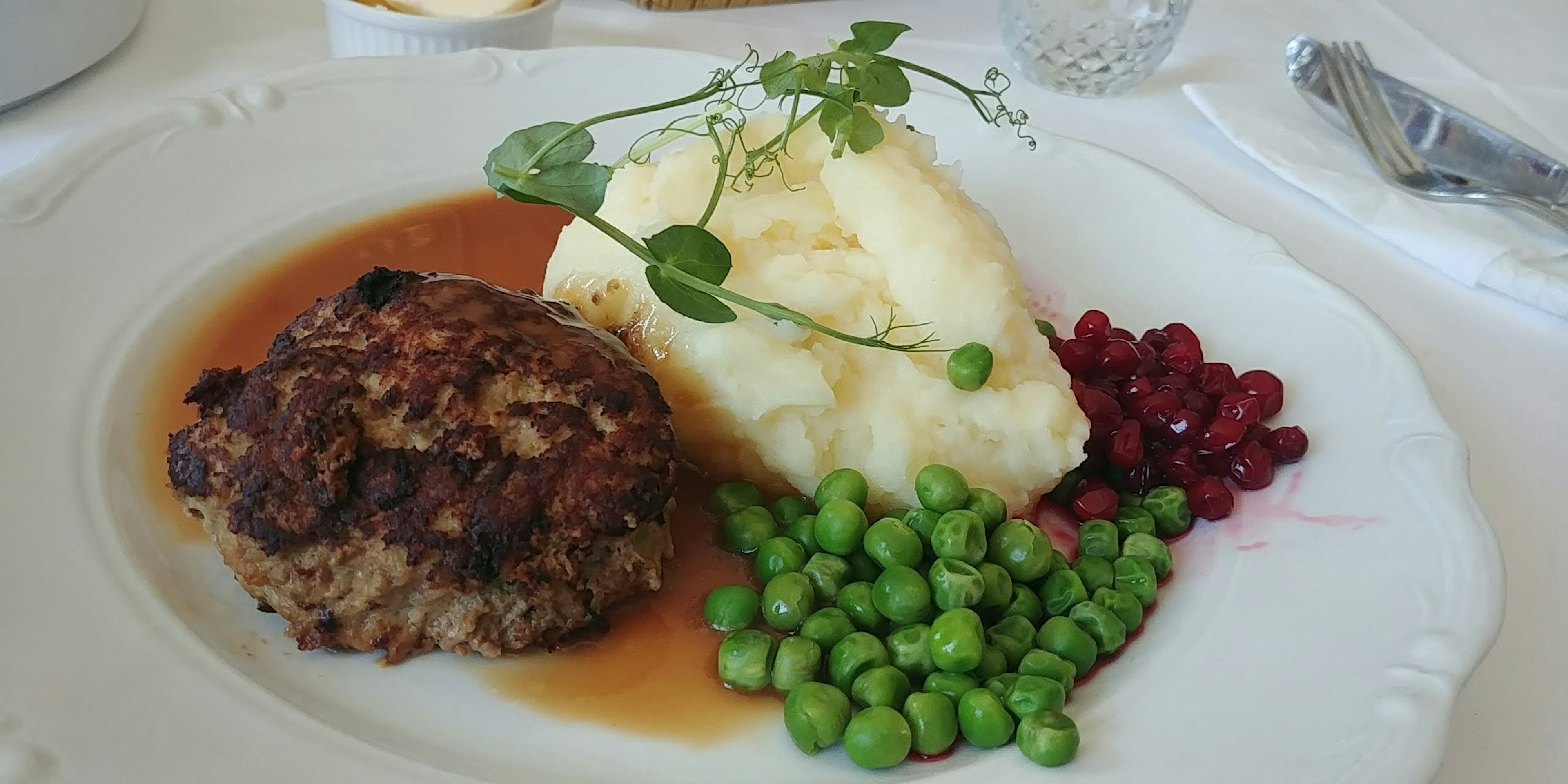 A plate featuring a hamburger steak mashed potatoes green peas and pomegranate seeds