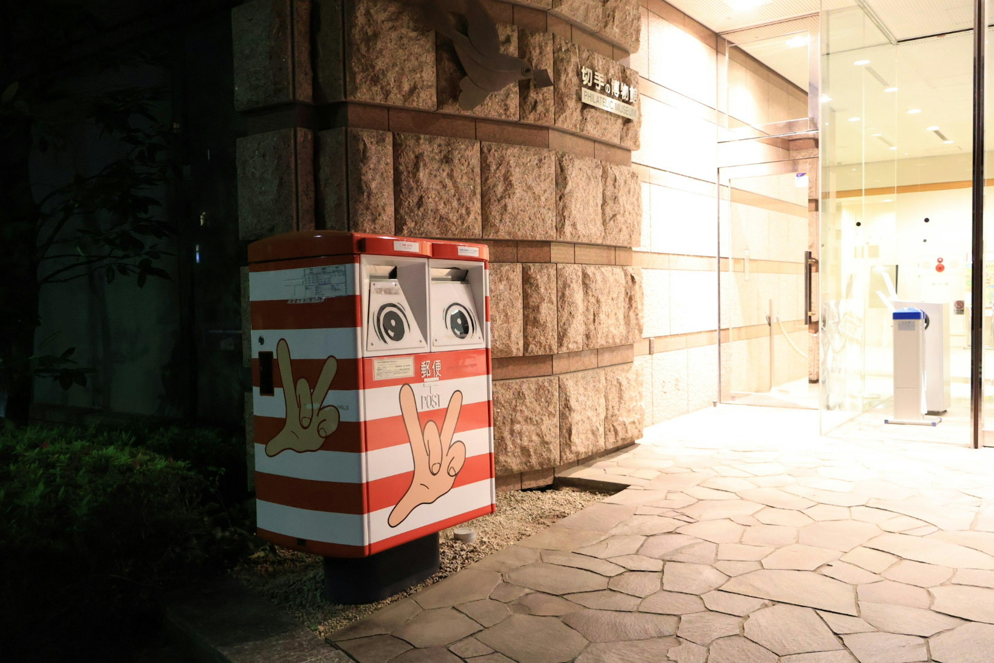 A striped mailbox with a smiling face standing at a street corner at night