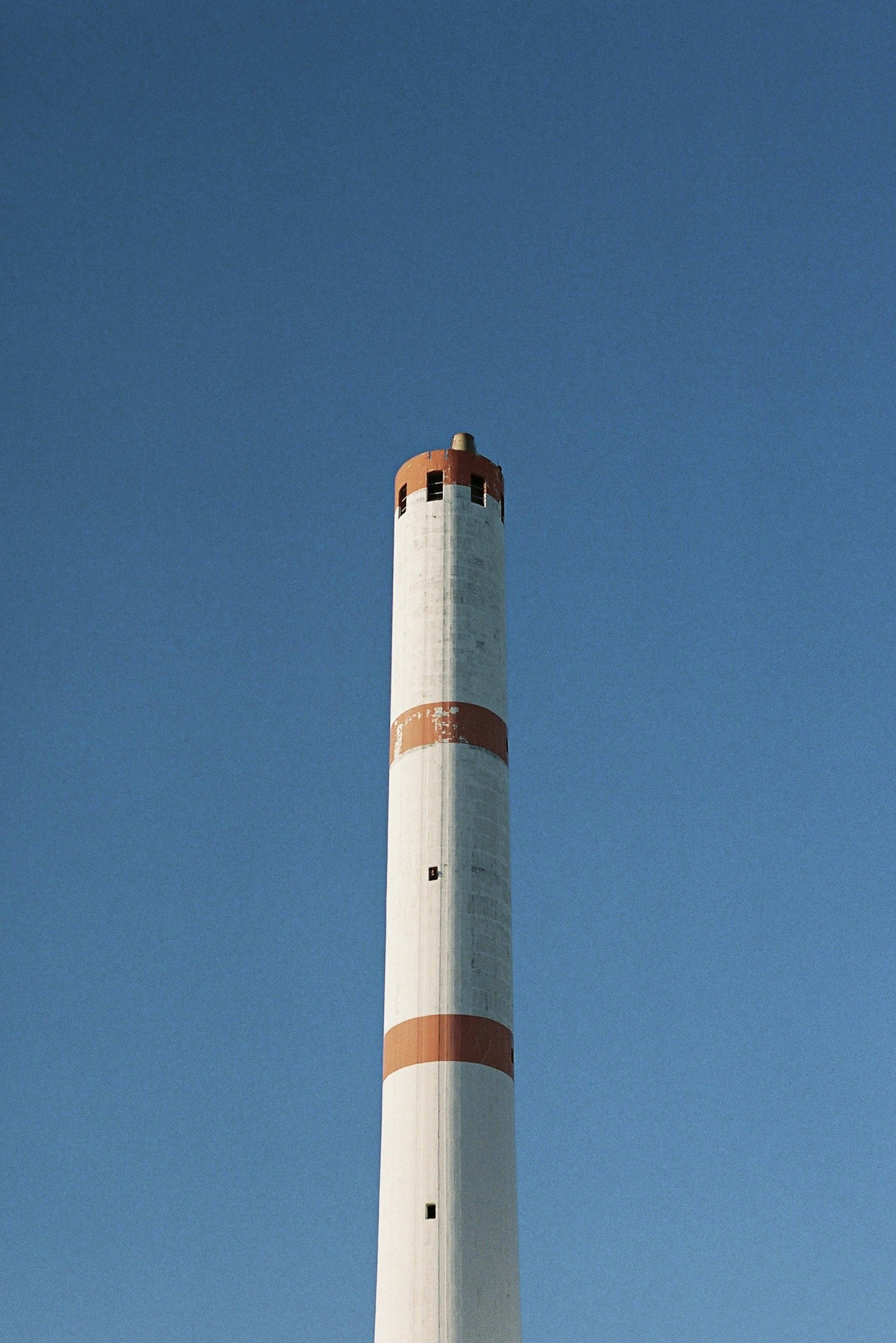 Tall white chimney with red stripes against a clear blue sky