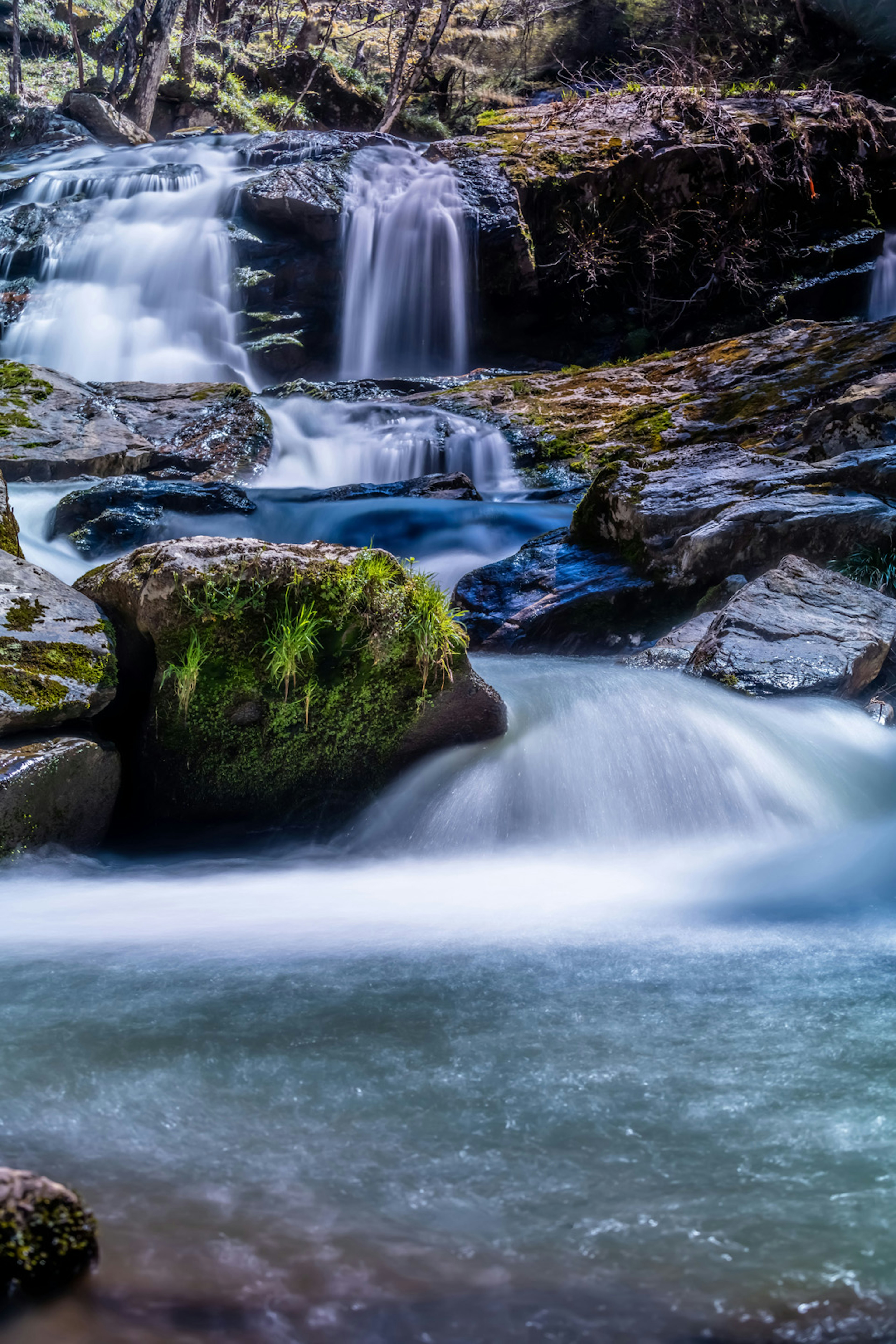 Grünmoosbedeckte Felsen umgeben von Wasserfällen und fließendem Wasser