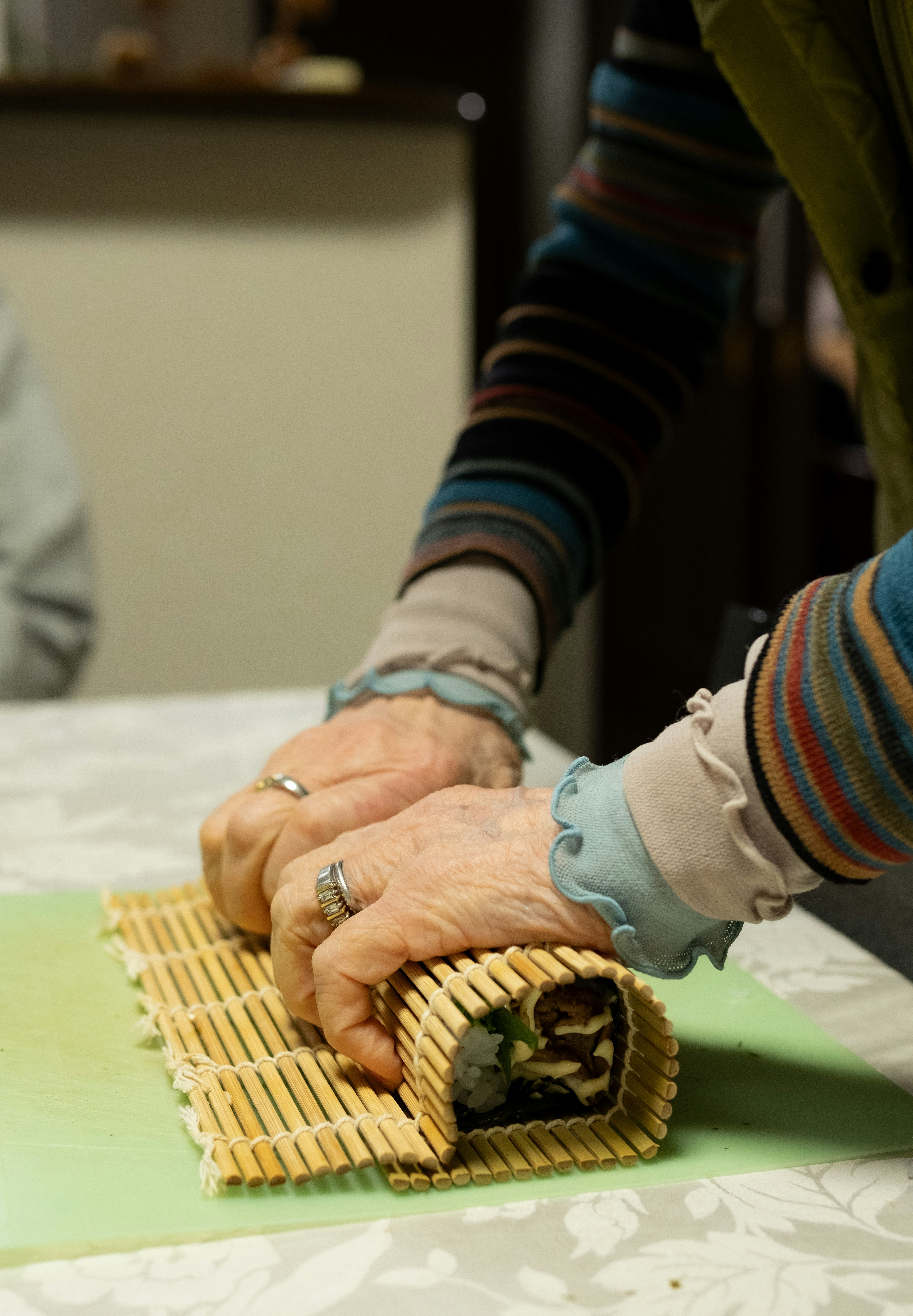 Hände, die Sushi mit einer Bambusmatte auf einem Tisch rollen