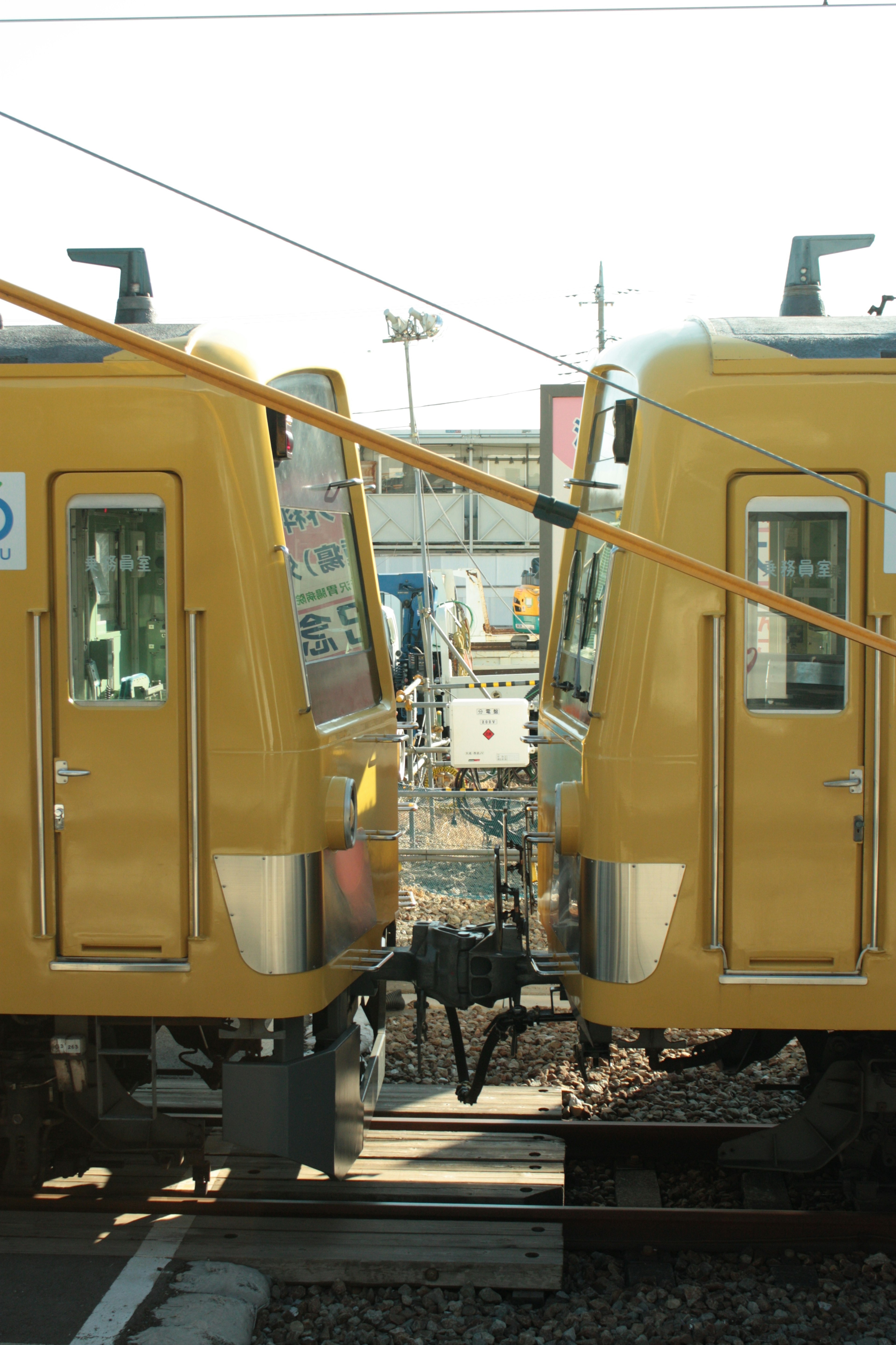 Dua kereta kuning saling berhadapan dengan rel dan sinyal di latar belakang