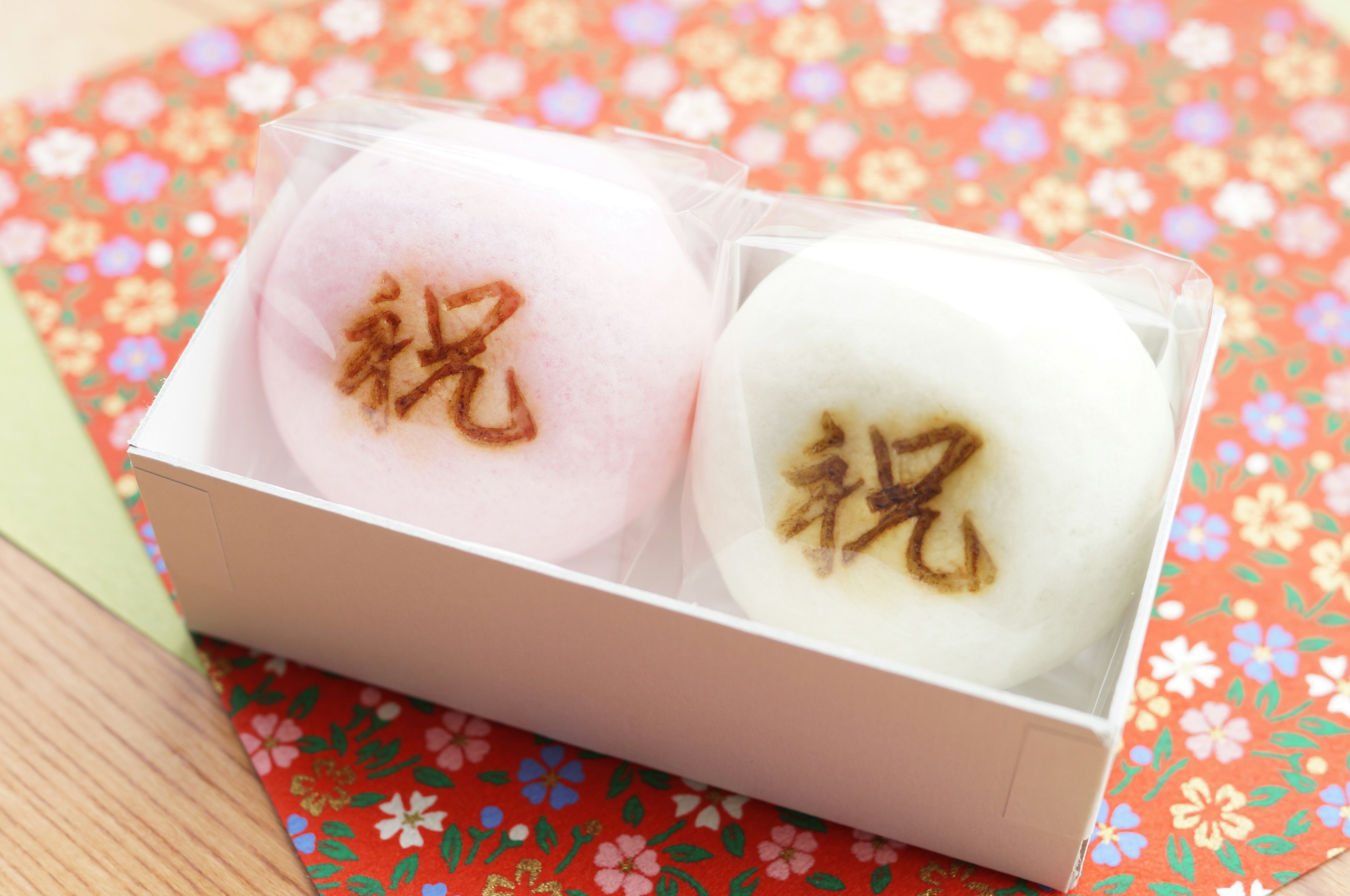 Dos dulces japoneses tradicionales en una caja rosa y blanca con escritura de celebración