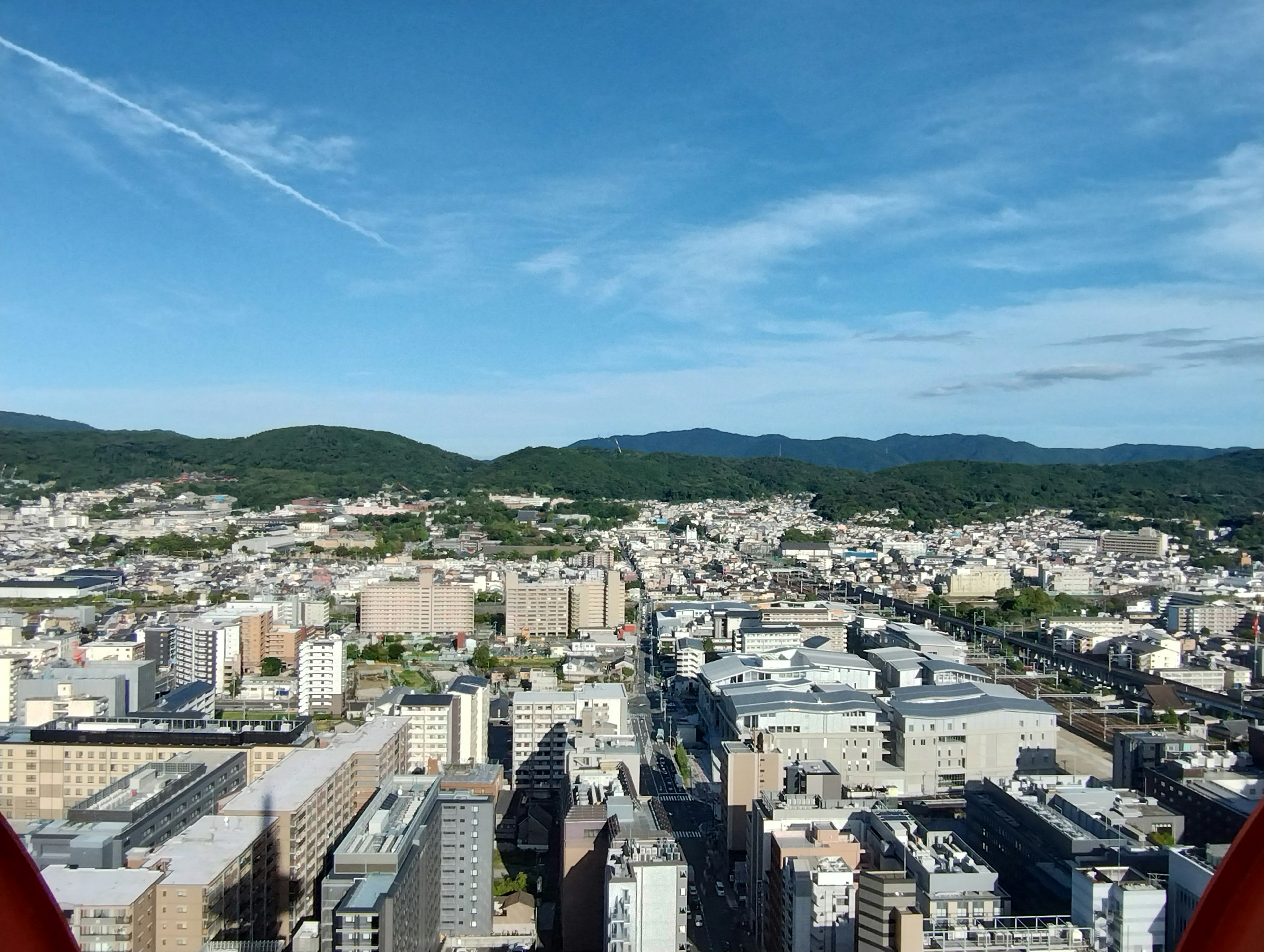 A panoramic view of a city from a high vantage point featuring green hills and a blue sky