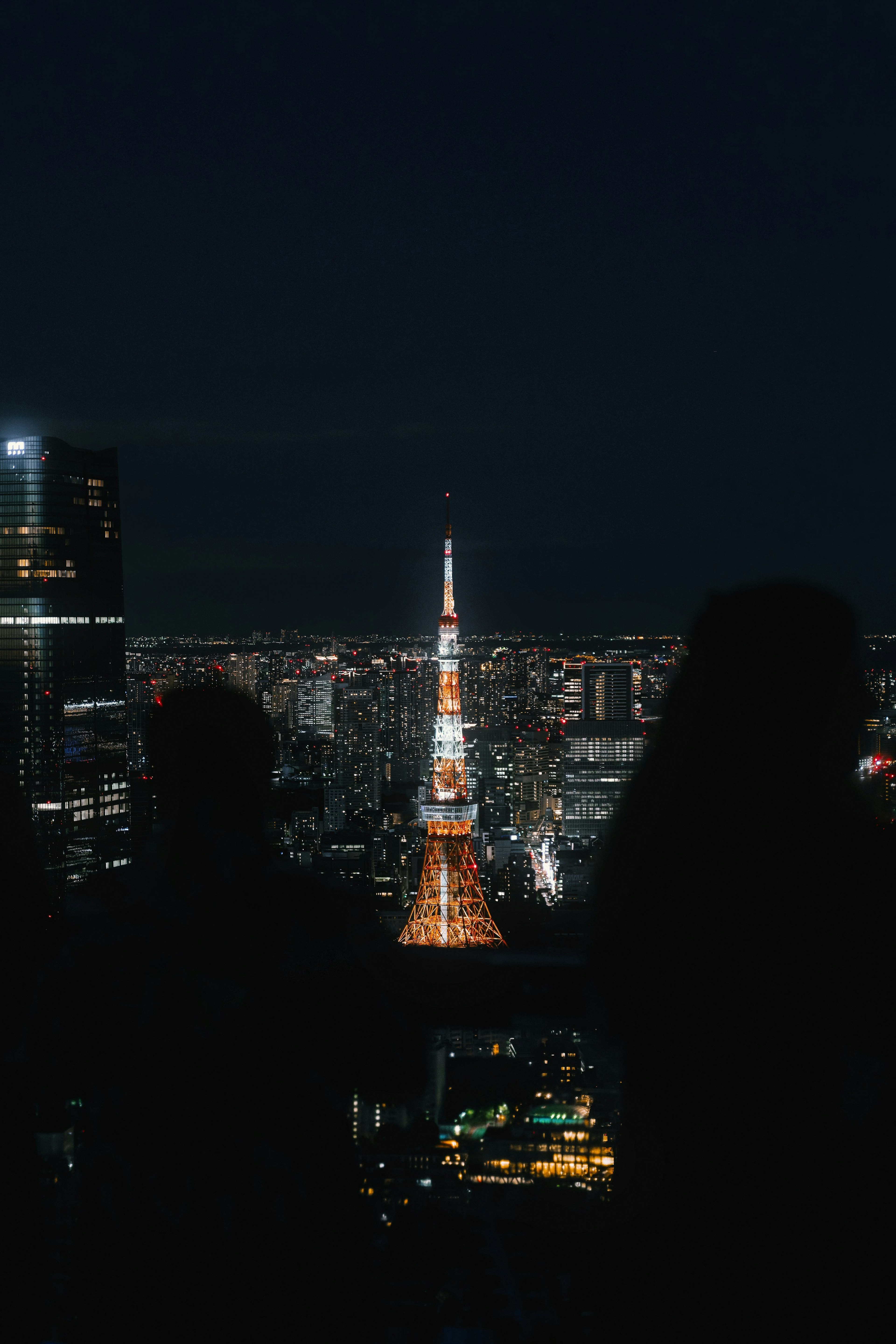 Siluet dua orang yang mengawasi Menara Tokyo di malam hari