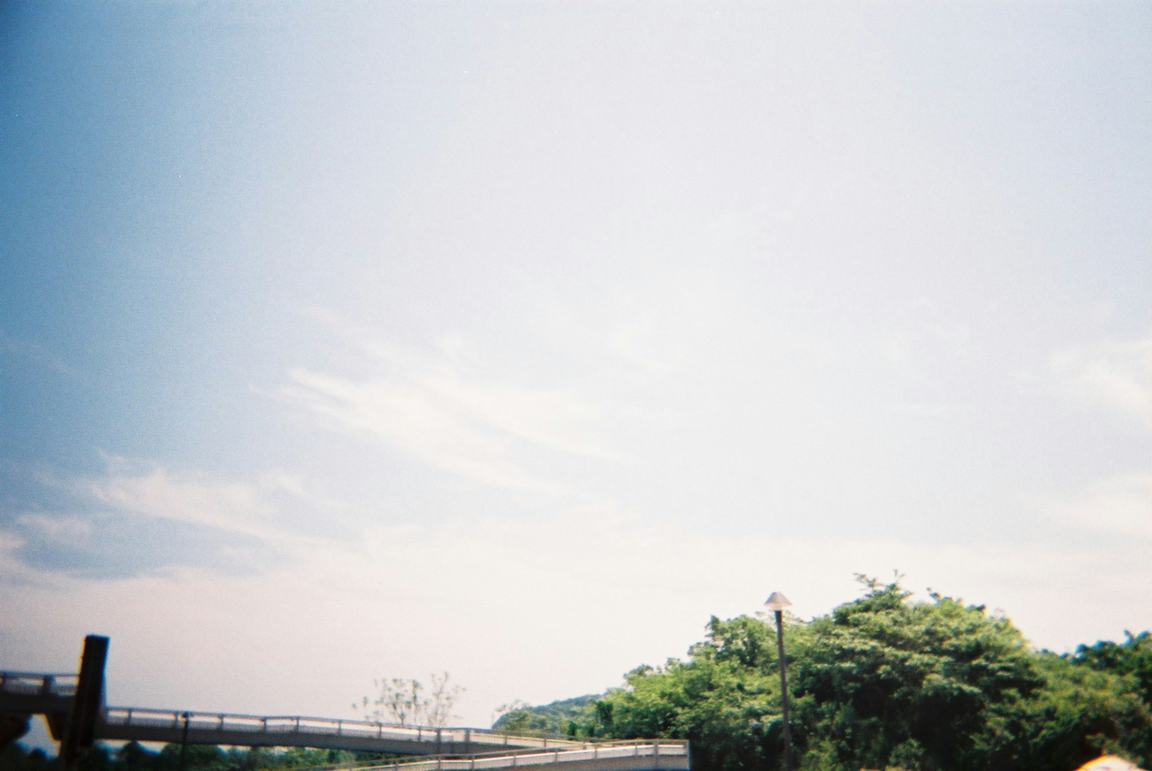 Eine Landschaft mit blauem Himmel und Wolken, die eine Brücke und grüne Bäume zeigt