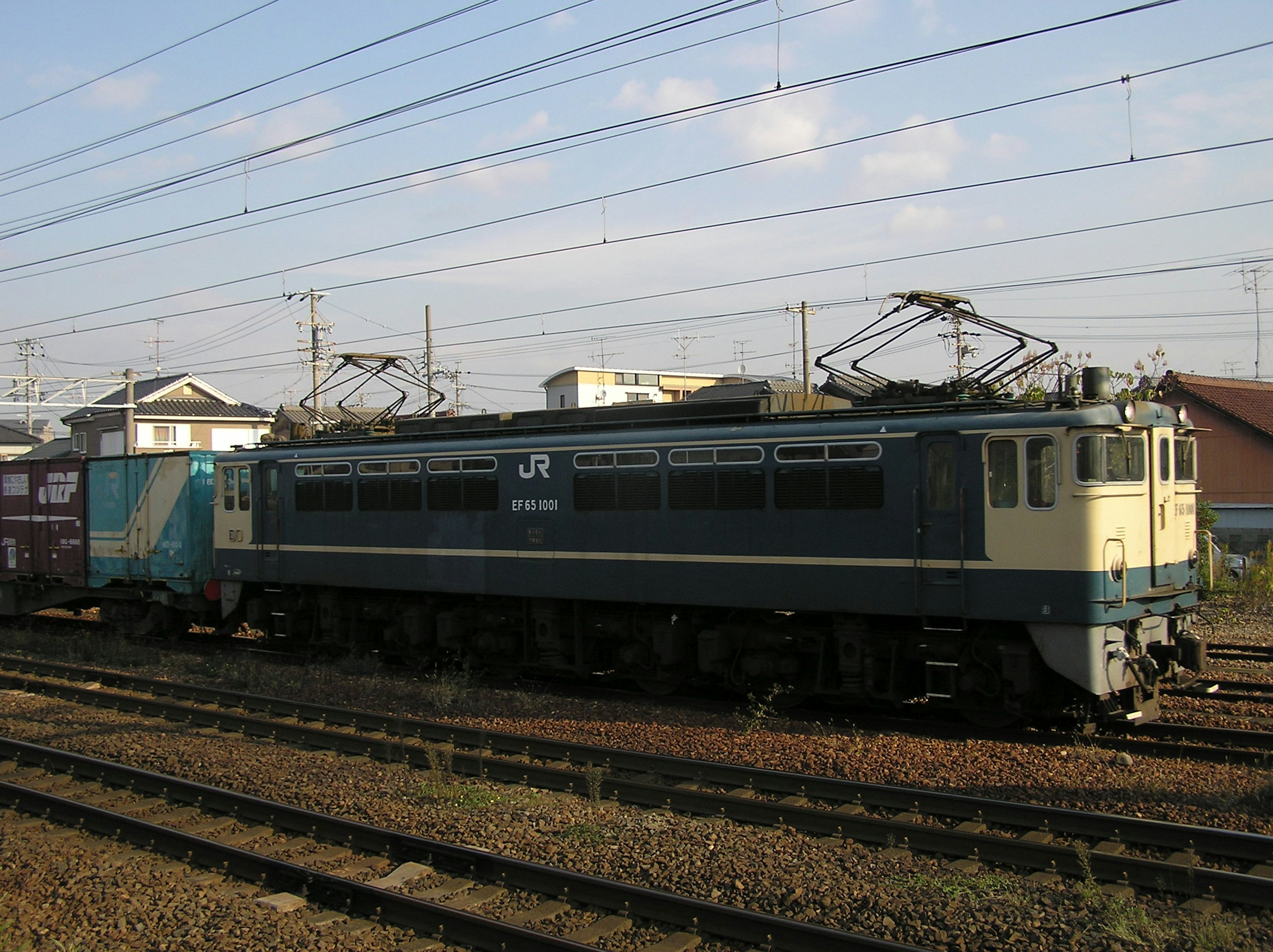 Blue and white electric locomotive parked on tracks with freight train