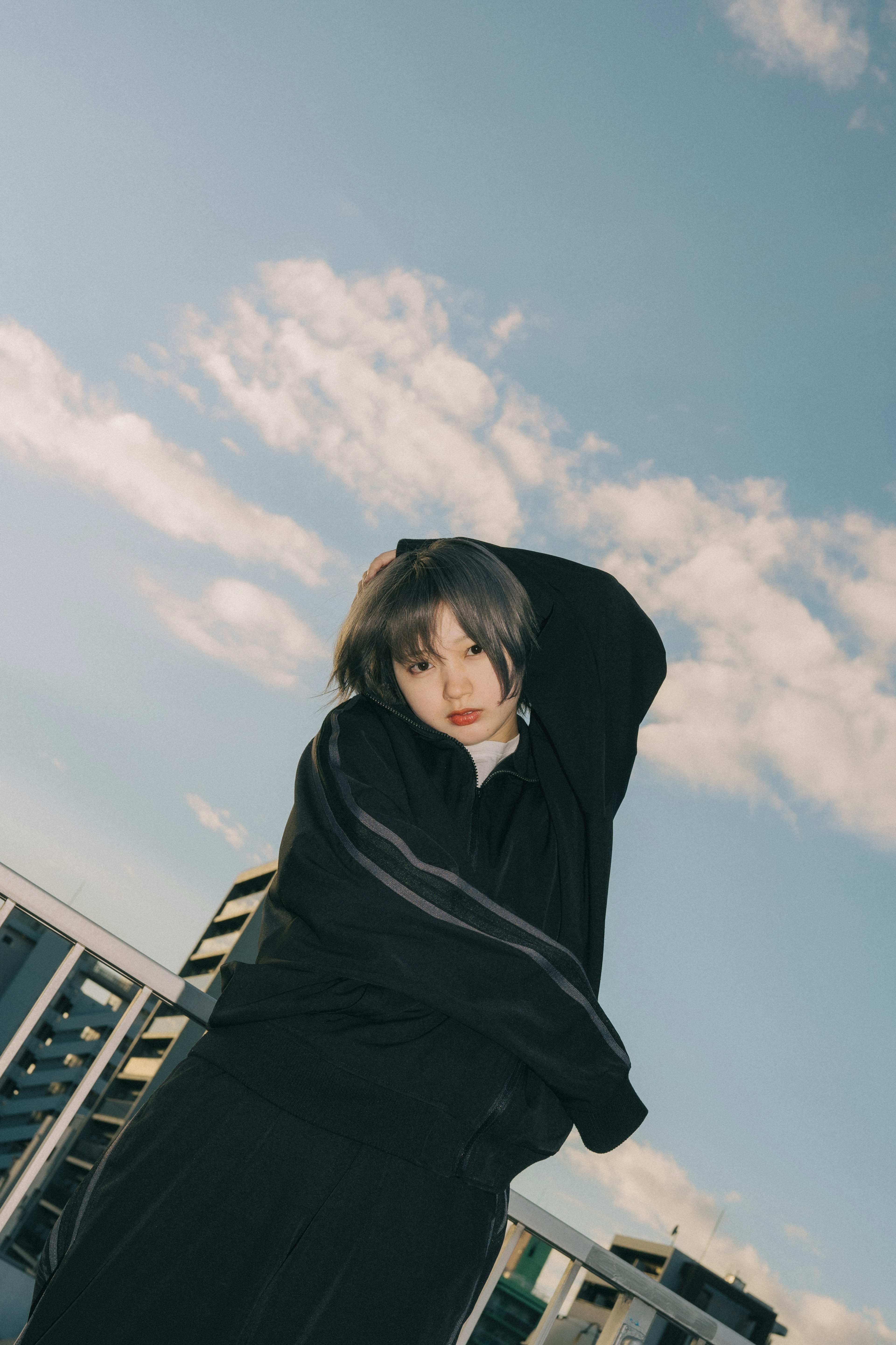 Modefoto einer Frau, die auf einem Dach posiert eleganter schwarzer Mantel vor blauem Himmel und Wolken