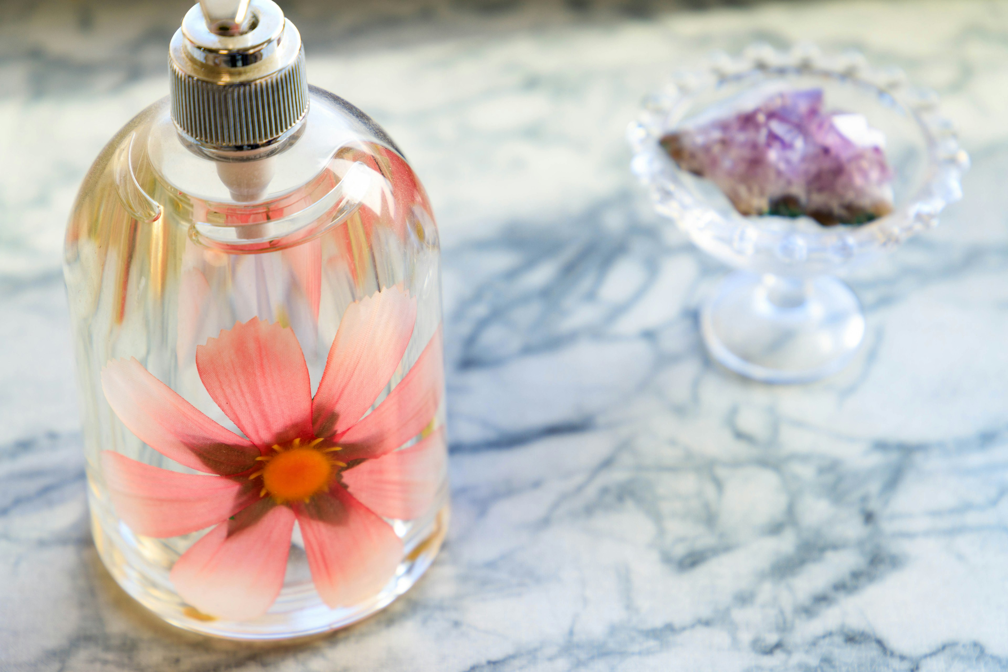 Botella de perfume transparente con una flor rosa en su interior colocada sobre una hermosa superficie de mármol