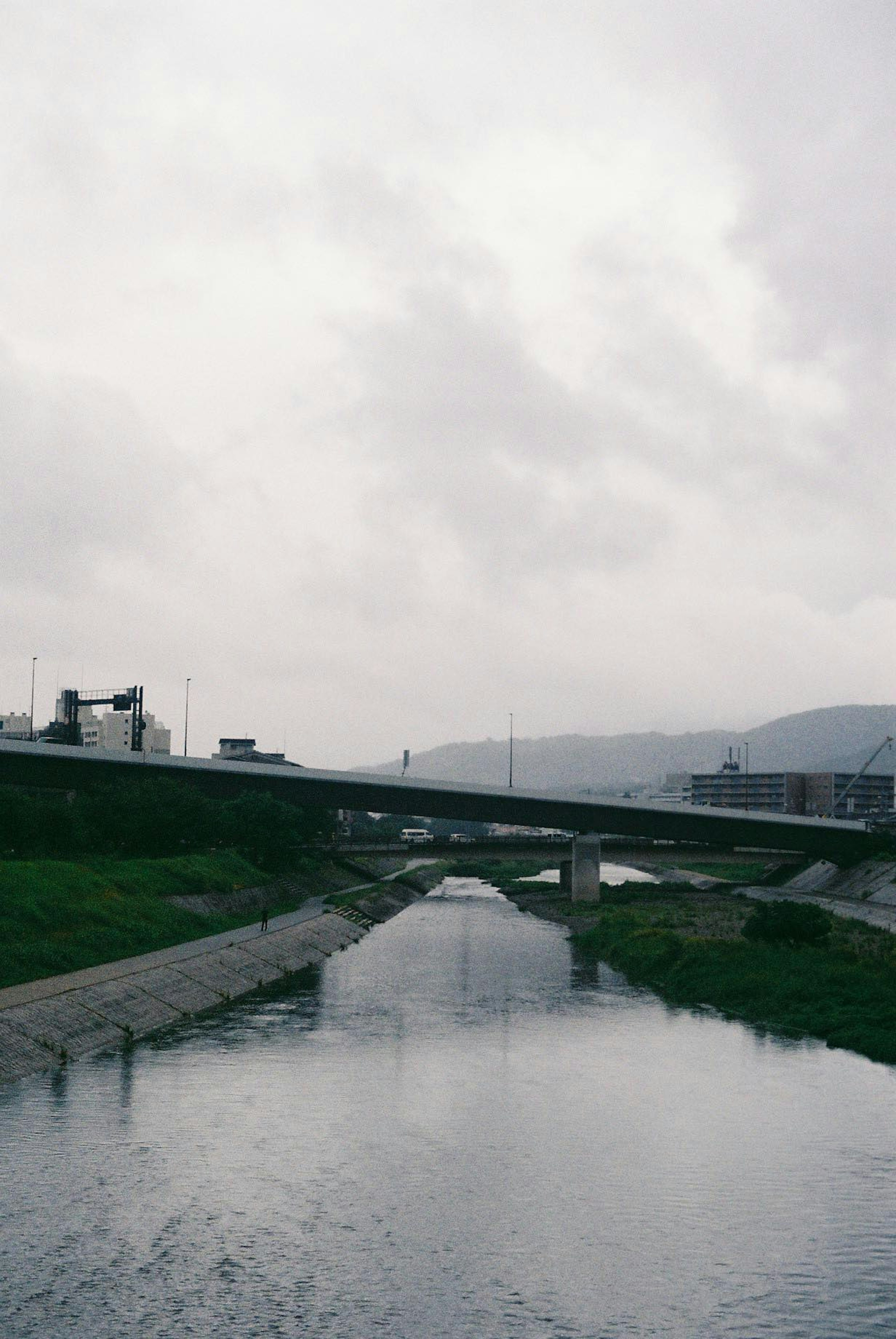 Pemandangan sungai dan jembatan di bawah langit mendung