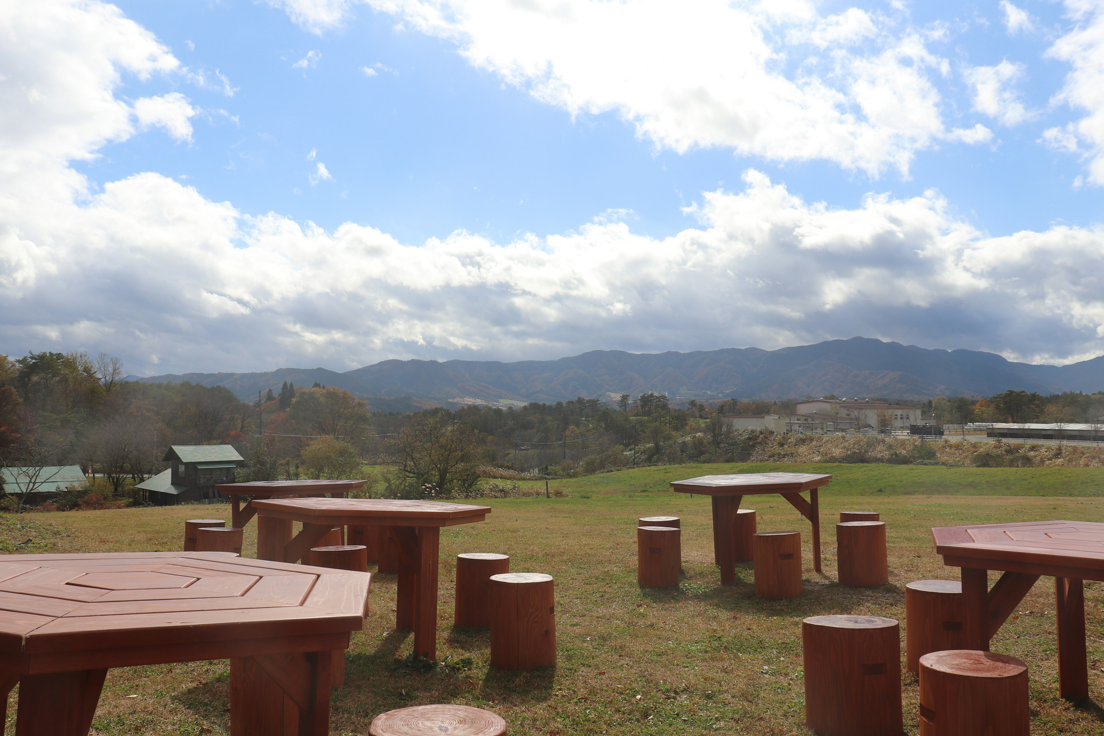 Geräumige grüne Wiese mit roten Holztischen und -hockern, die auf entfernte Berge und blauen Himmel blicken