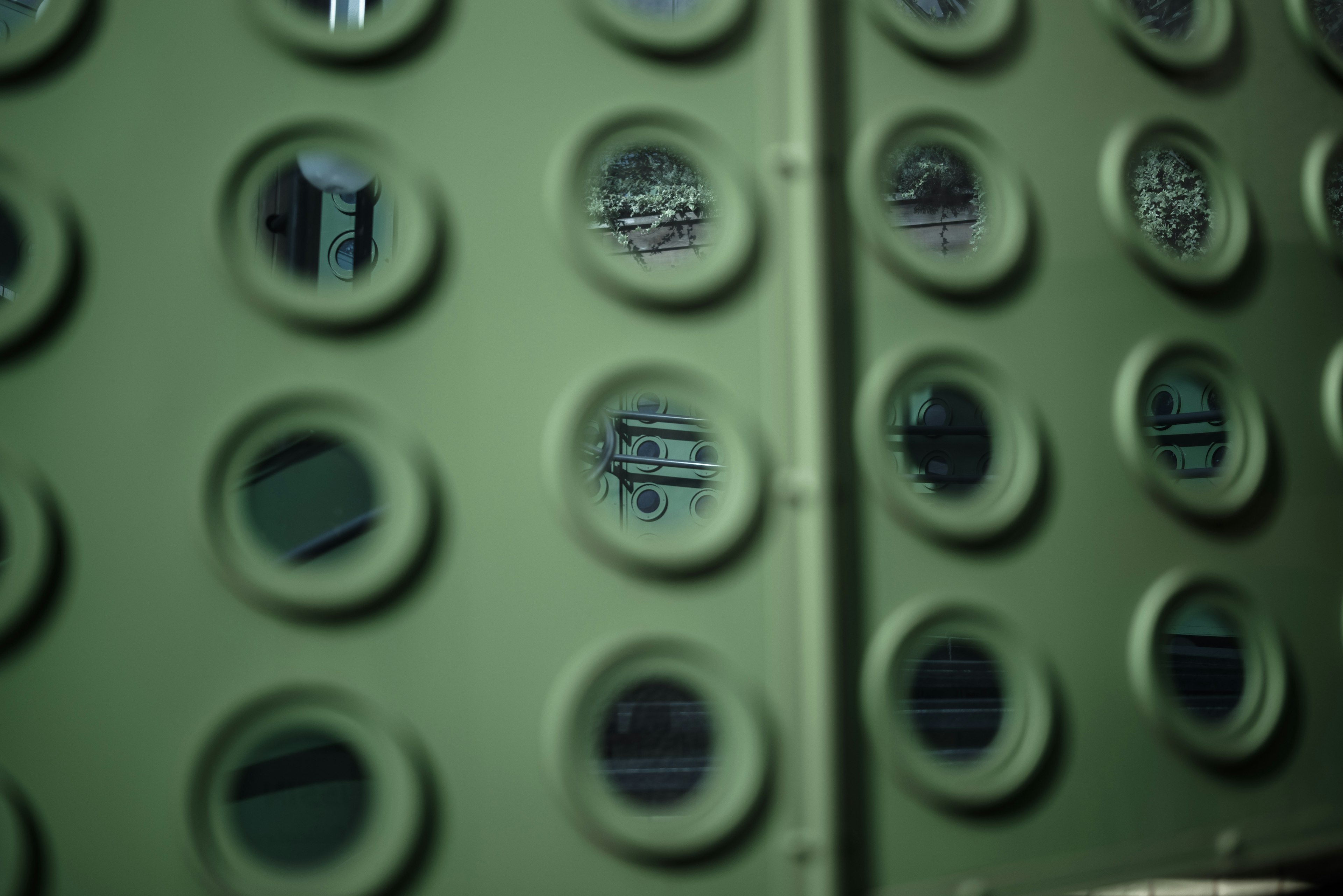 Green wall with circular holes revealing a blurred view of objects behind