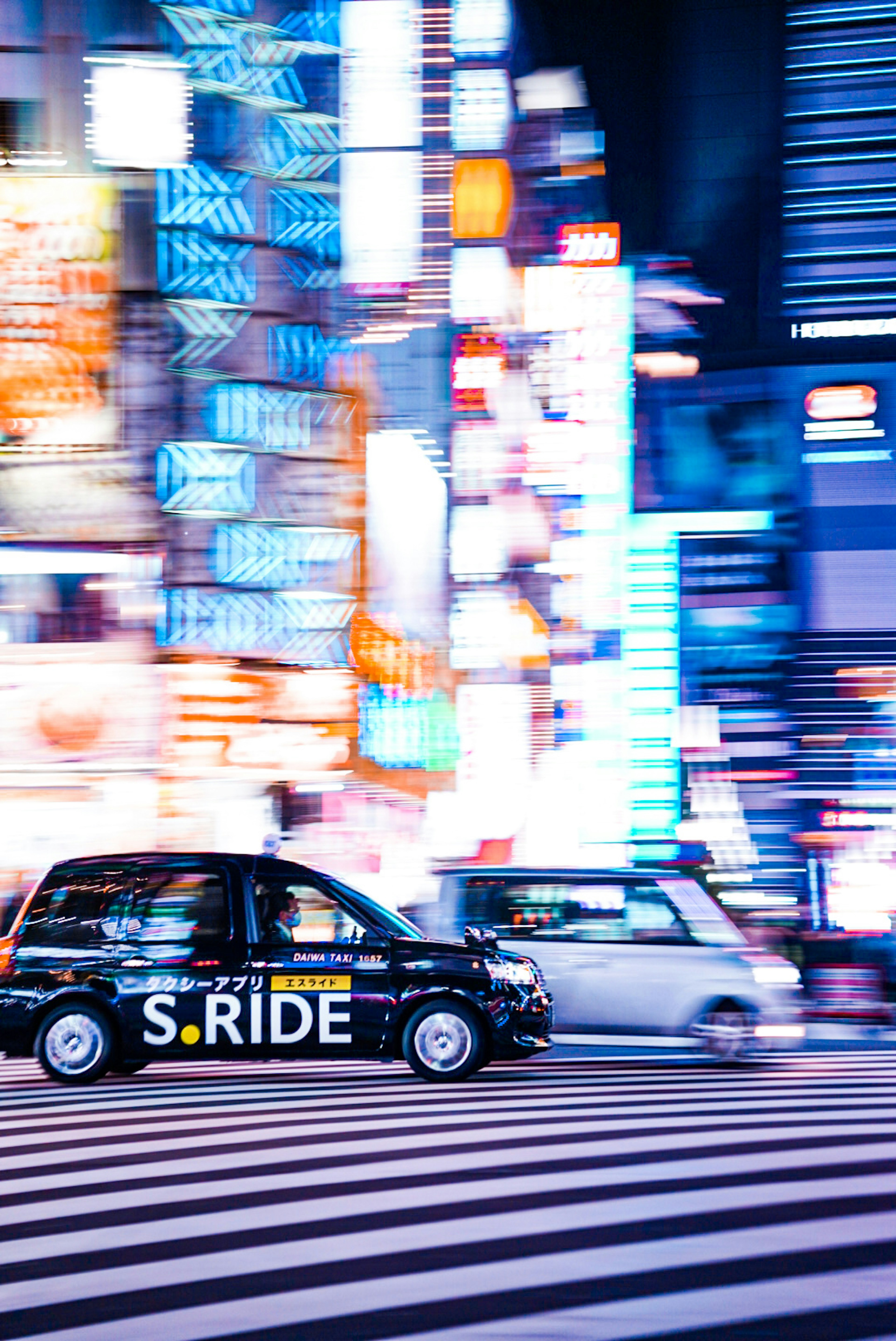 Taxi che attraversa una vivace strada di Tokyo con luci al neon di notte