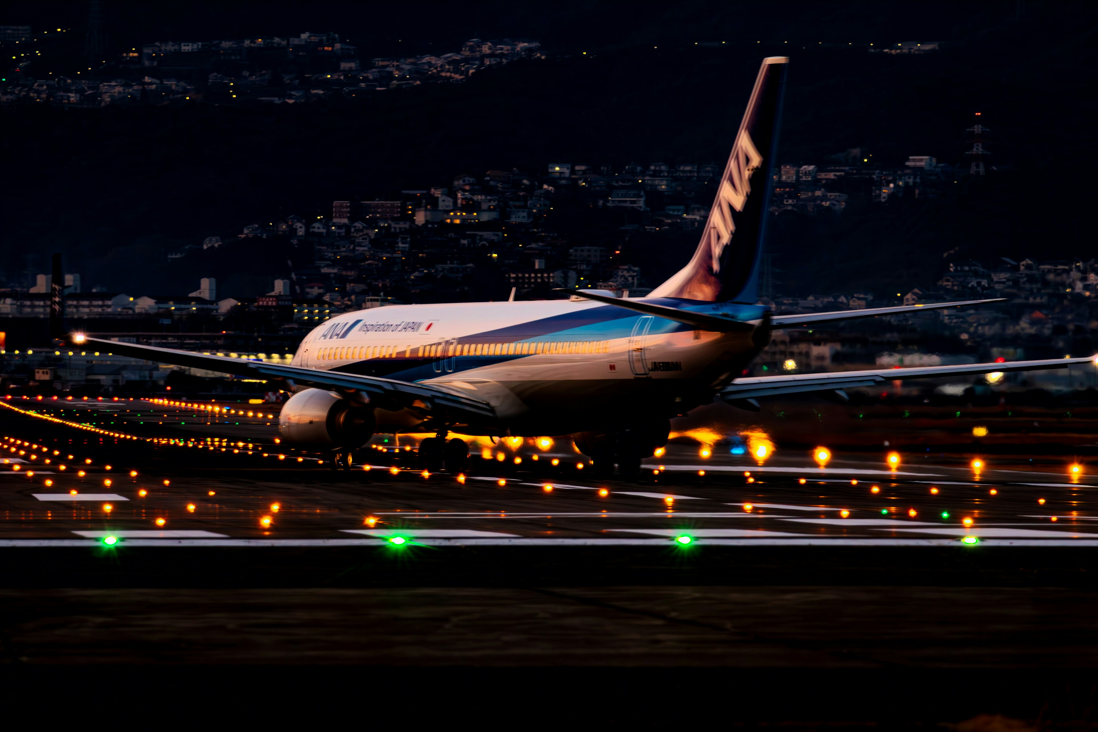 Avión rodando en una pista de noche con luces de la ciudad de fondo