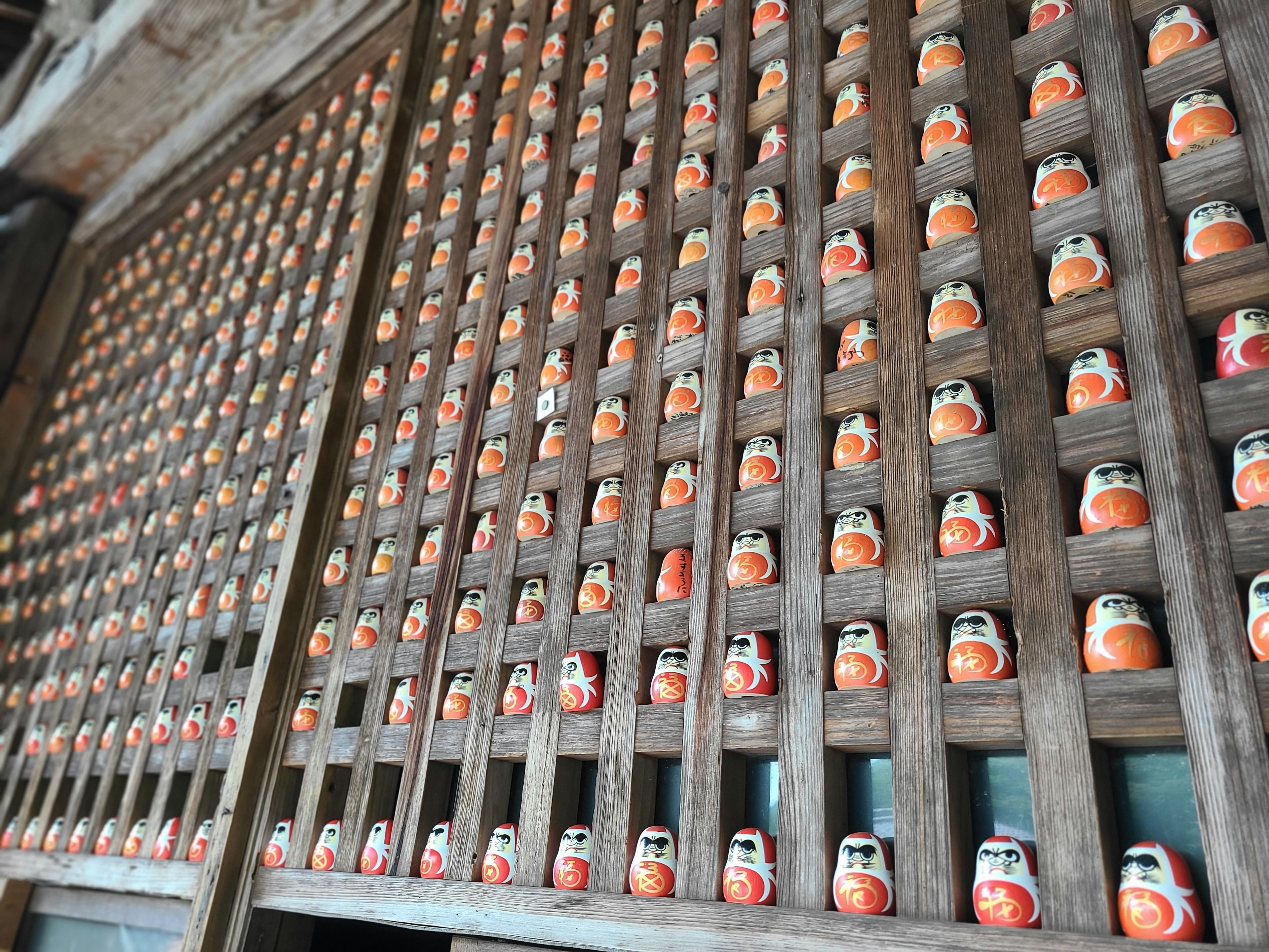 Eine Holzwand mit ordentlich angeordneten orangen Daruma-Puppen