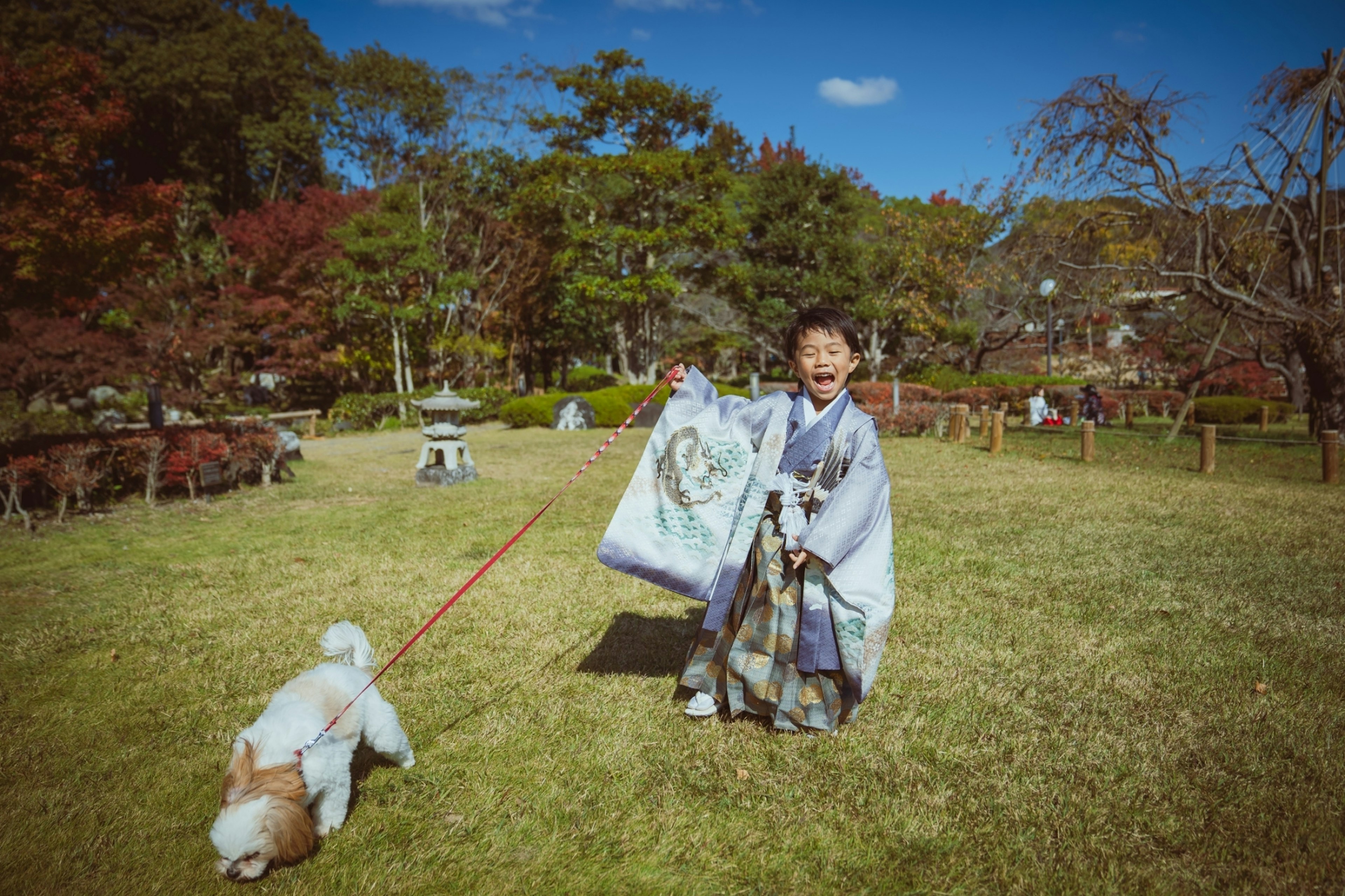 Ein Kind in einem Kimono, das einen Hund in einem Park spazieren führt