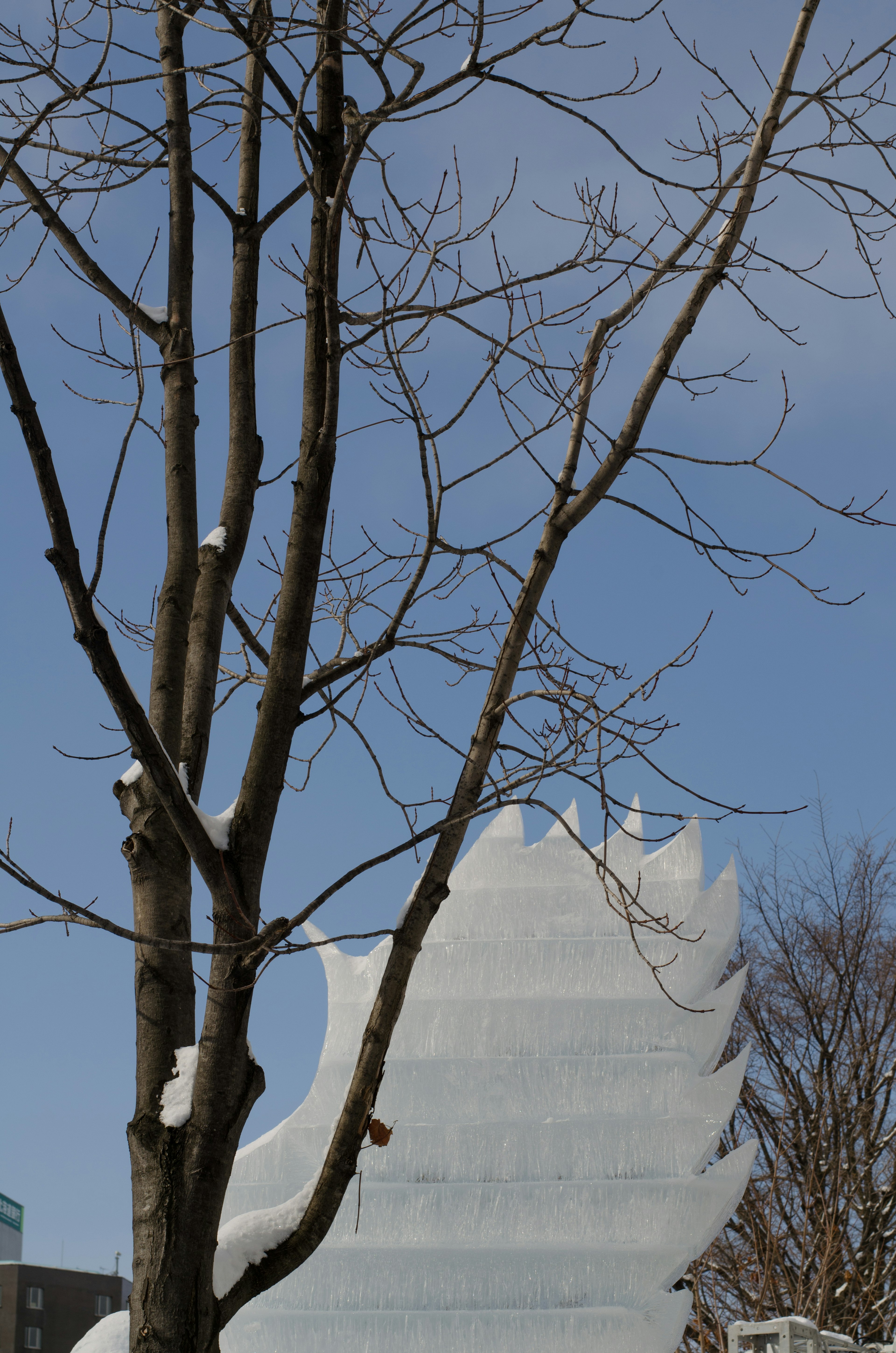 Un arbre aux branches nues à côté d'une sculpture de neige sous un ciel d'hiver