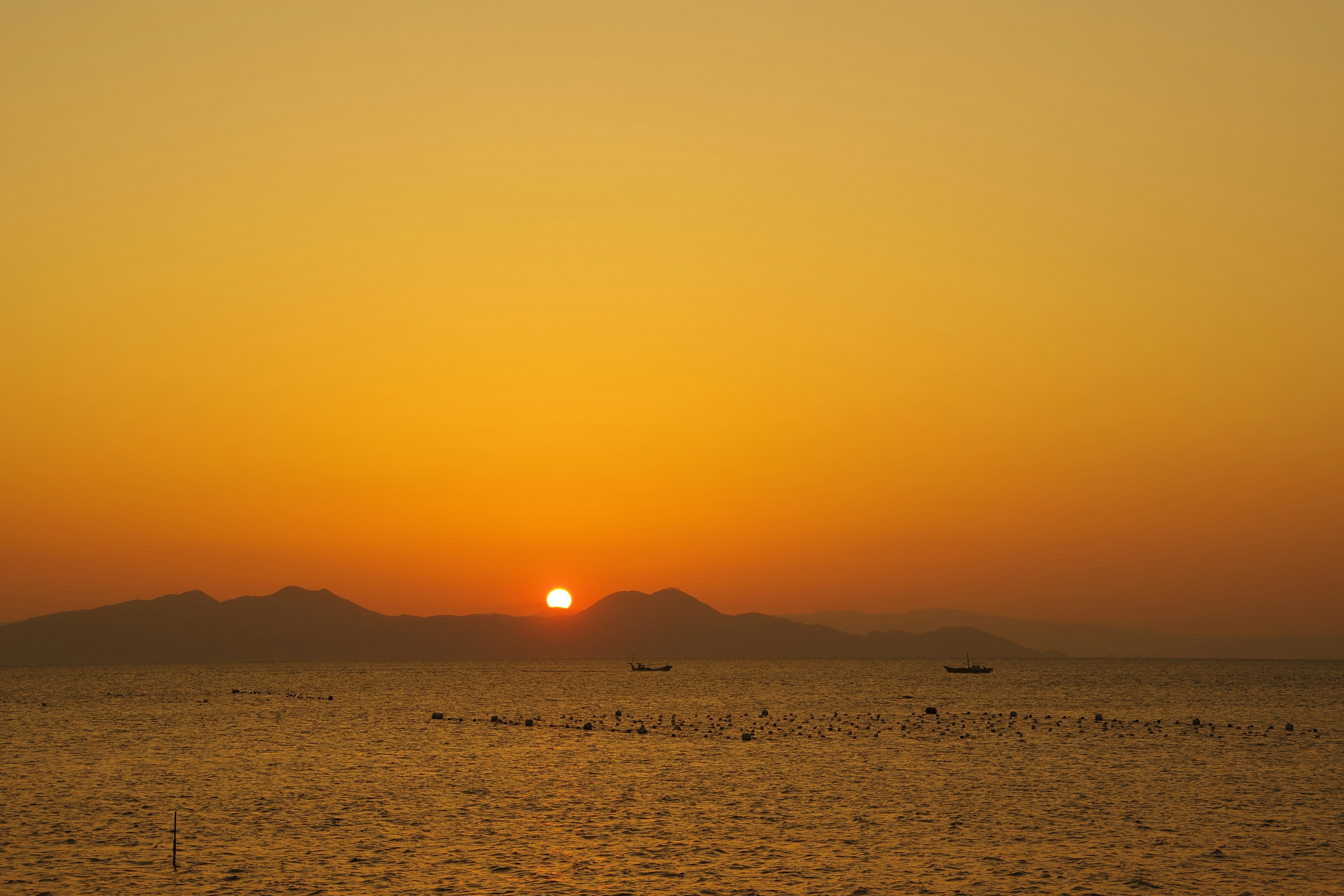 夕陽在橙色天空中落入海洋，山的輪廓