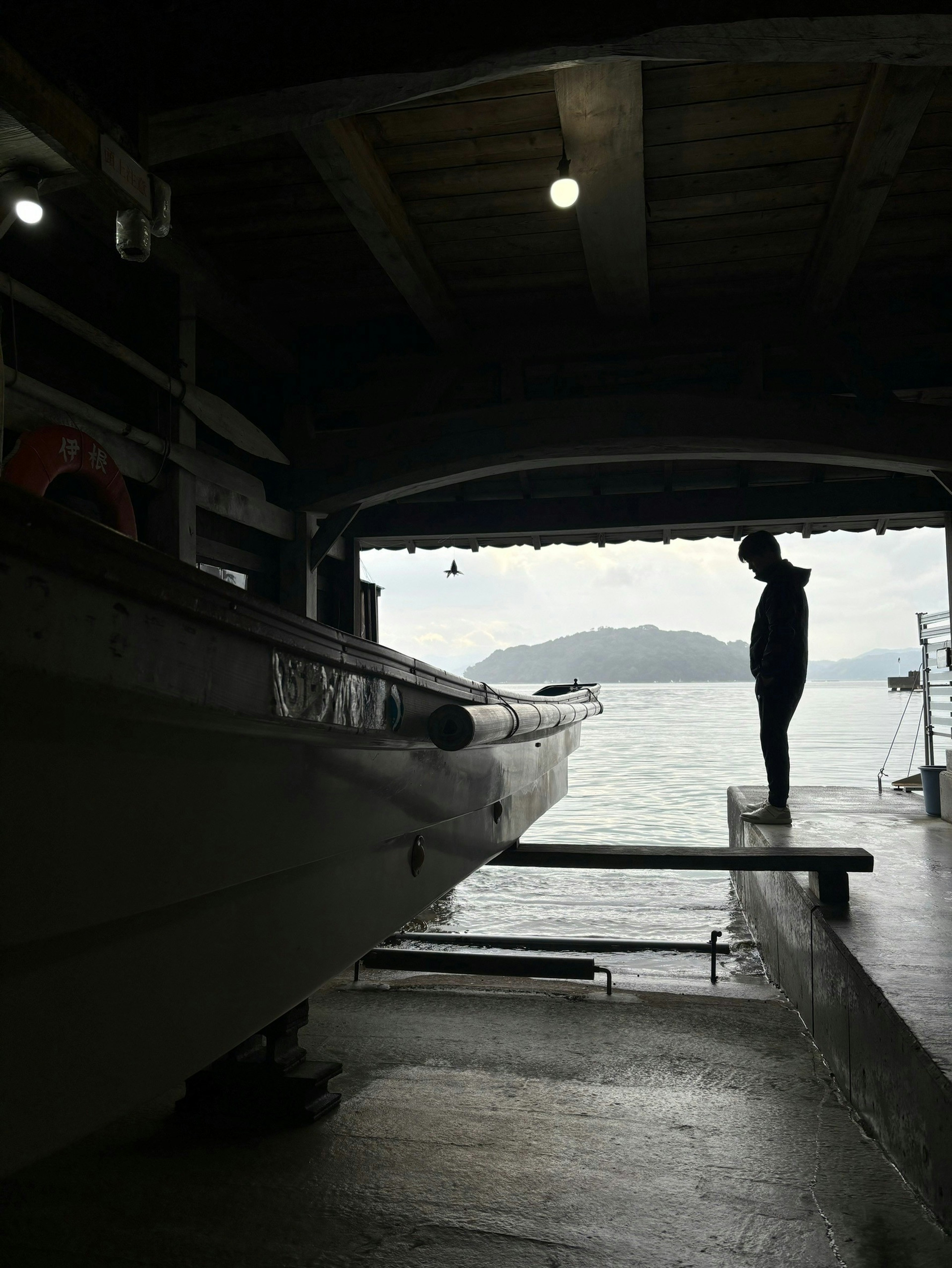 Silhouette einer Person neben einem Boot mit dem Meer im Hintergrund