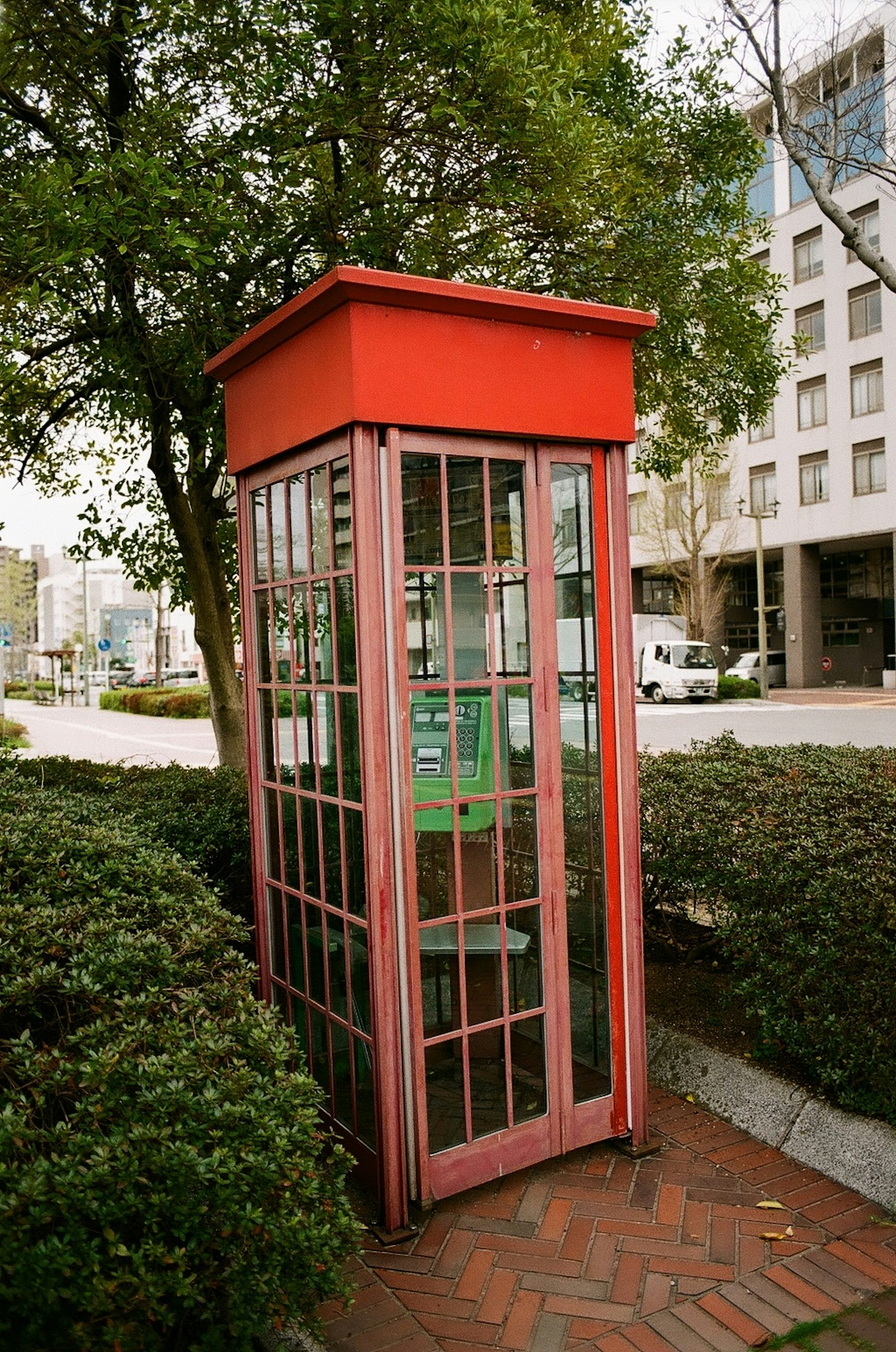 Telefonzelle mit rotem Dach umgeben von grünen Büschen