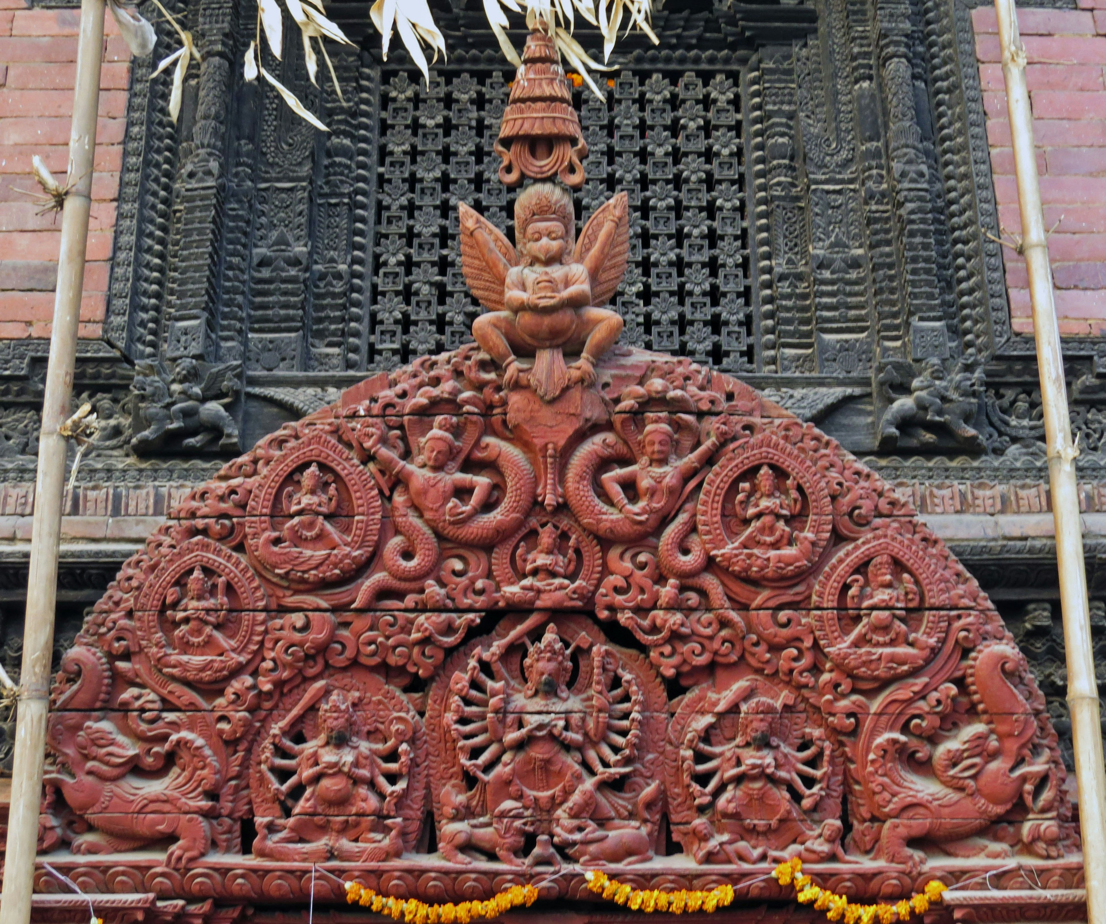 Décoration sculptée rouge au sommet d'une porte de temple avec une figure d'ange et plusieurs divinités