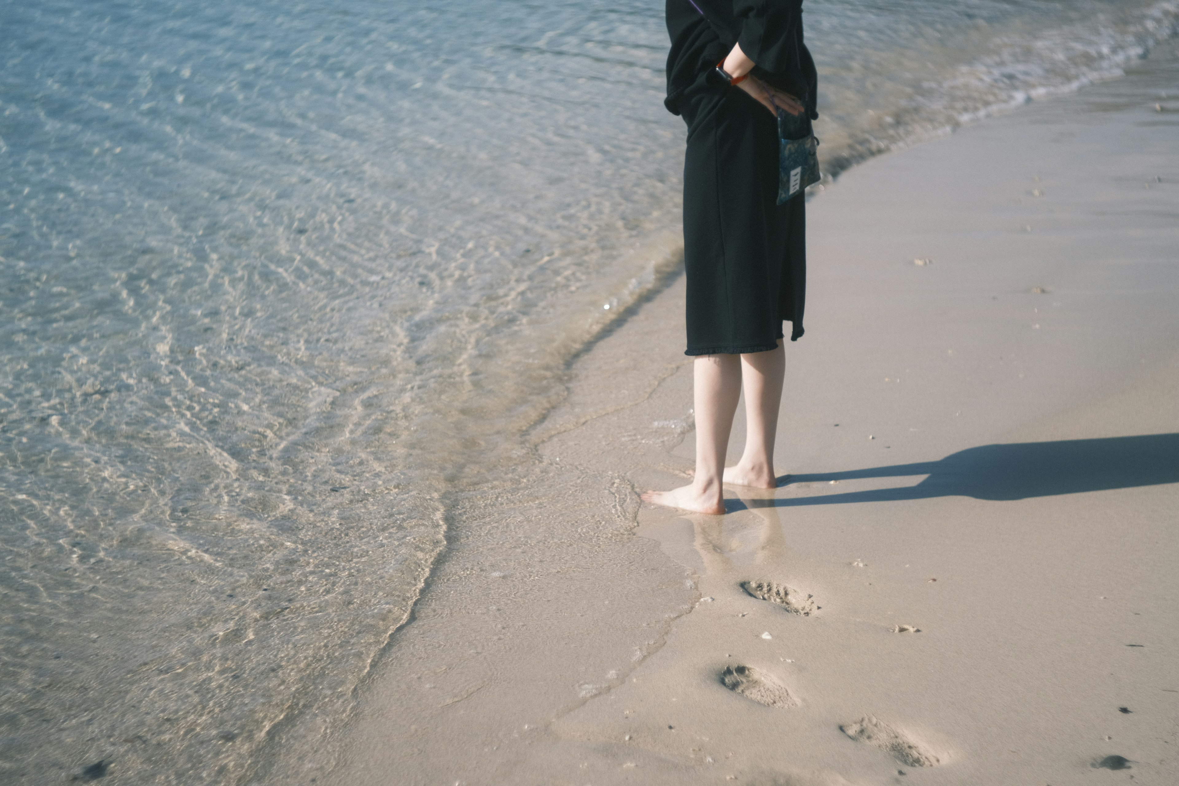 Woman standing at the beach with waves lapping at her feet