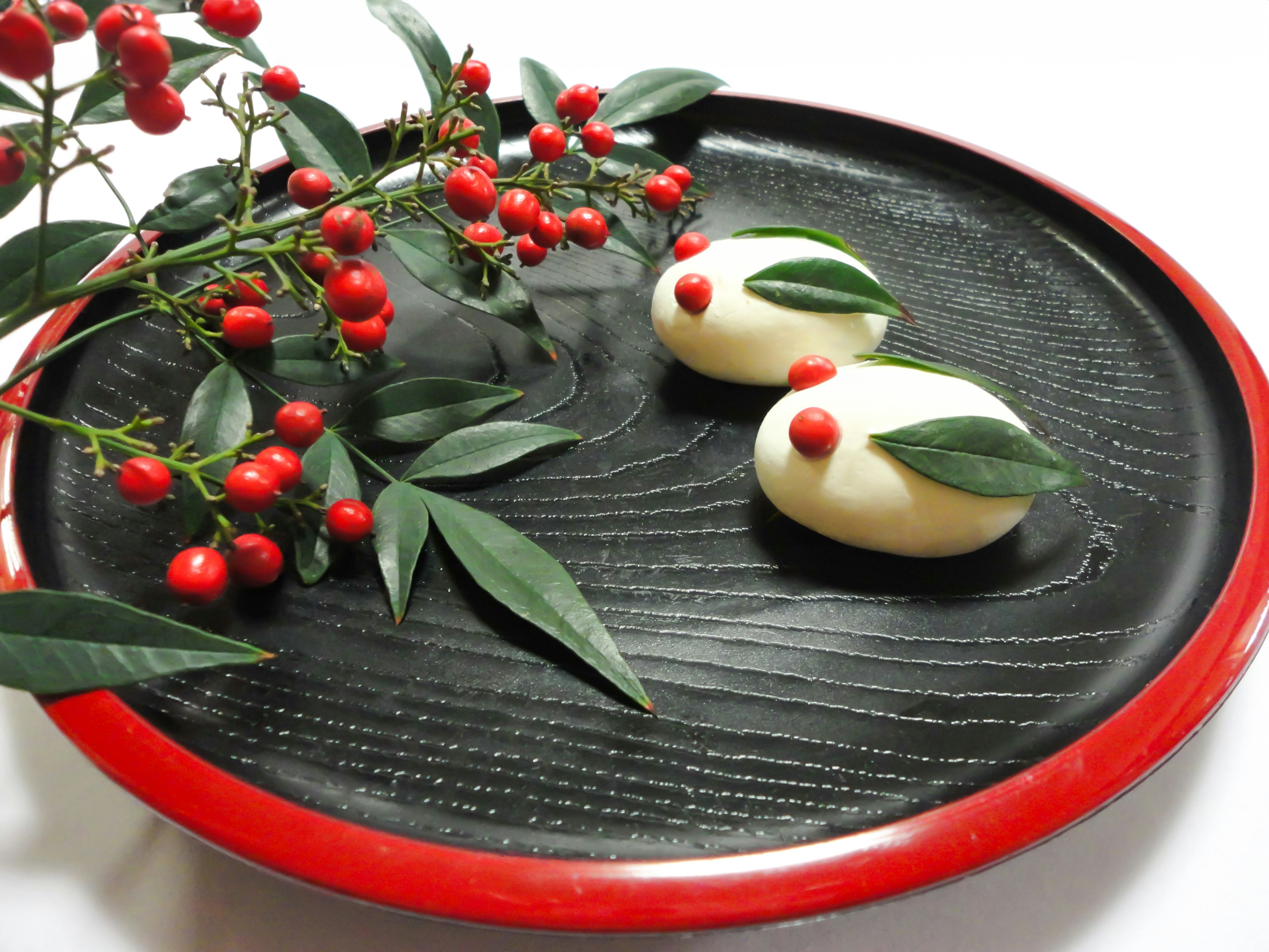 Bonbons japonais en forme d'oiseaux sur une assiette noire avec des baies rouges et des feuilles