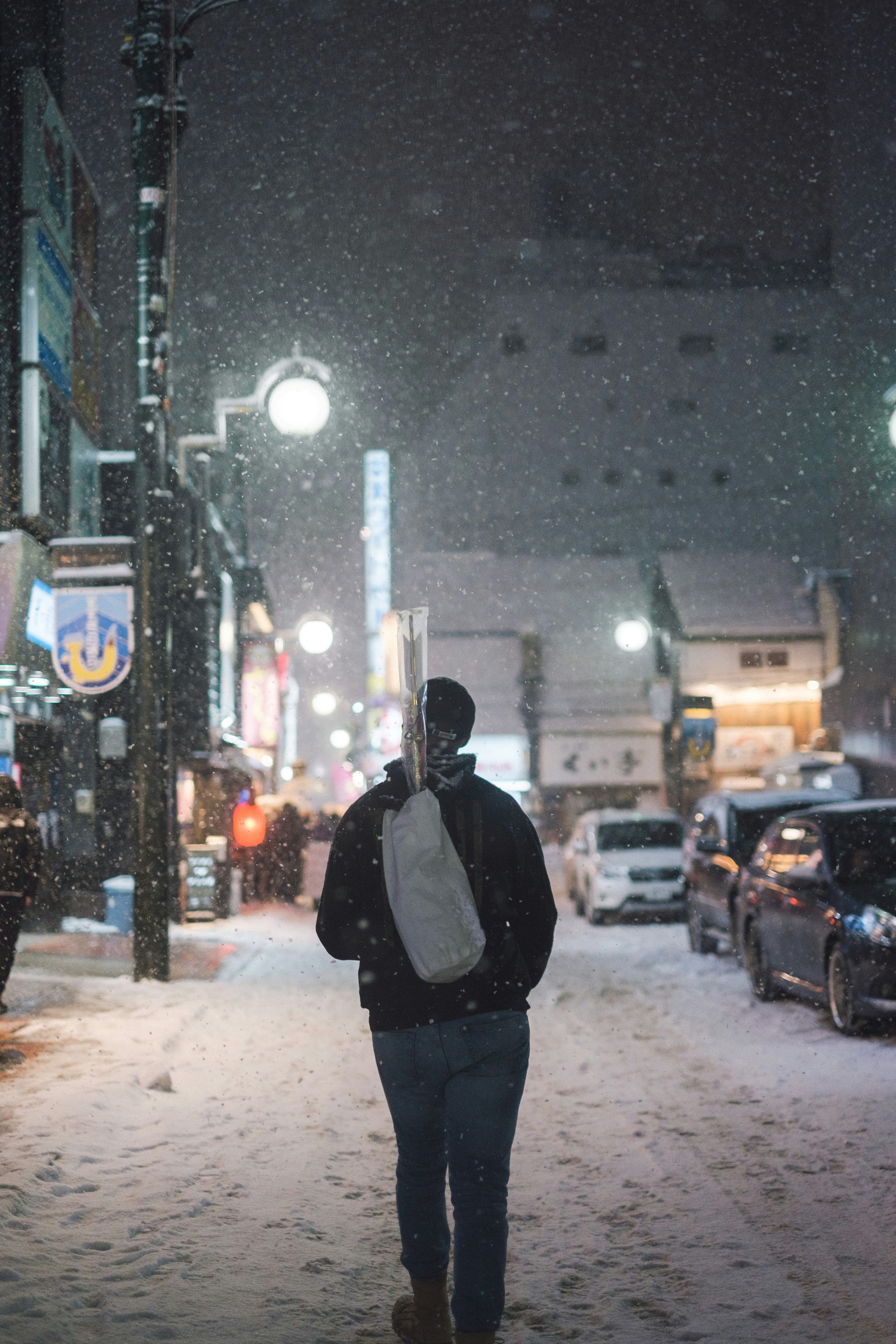 雪の中を歩く男性の後ろ姿 街灯が照らす夜の通り