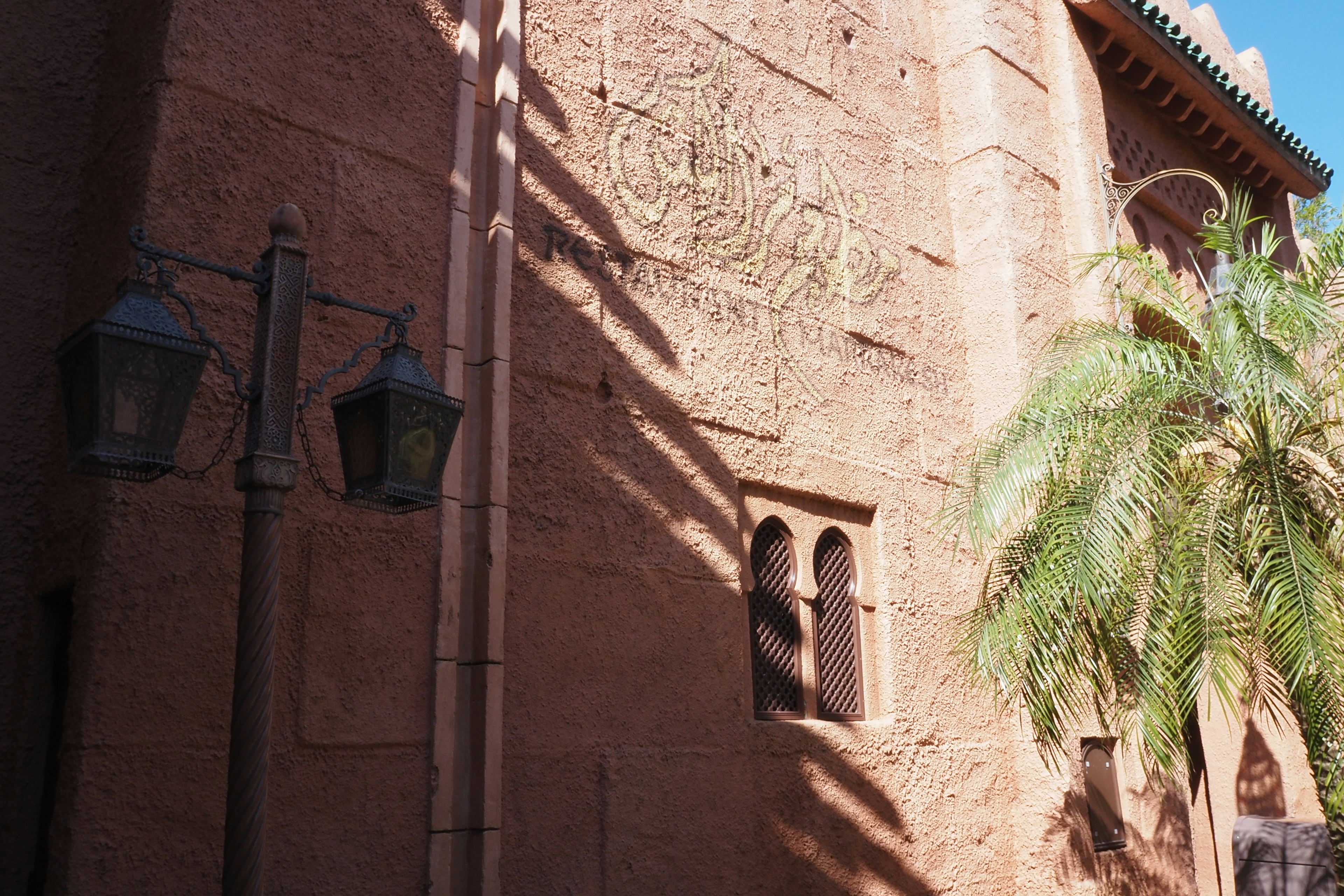 Side view of a building with reddish-brown walls featuring a window and palm trees