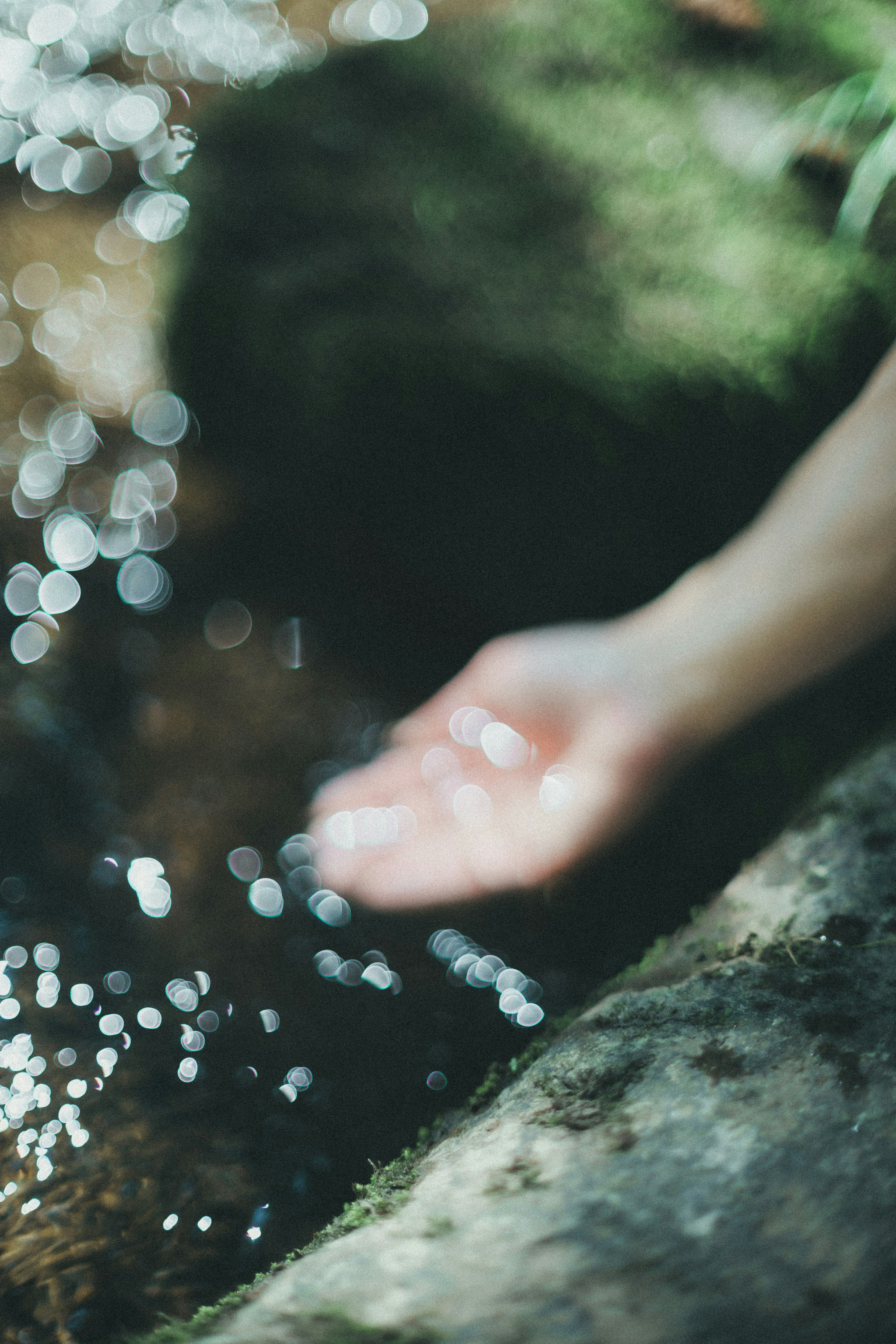 Una mano alcanzando un arroyo con gotas de agua brillantes en un fondo borroso