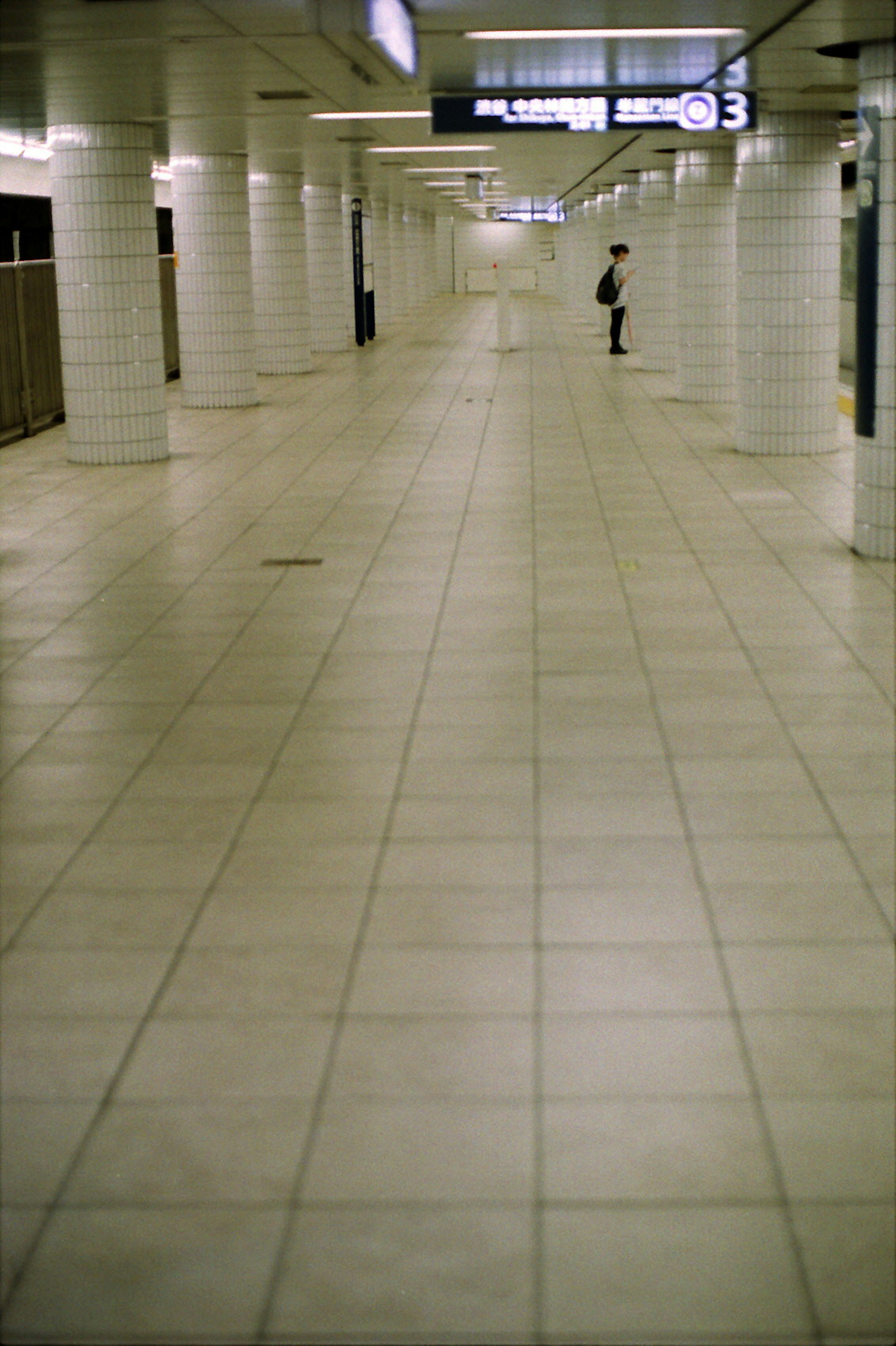 Spacious white tiled underground corridor with a lone figure standing