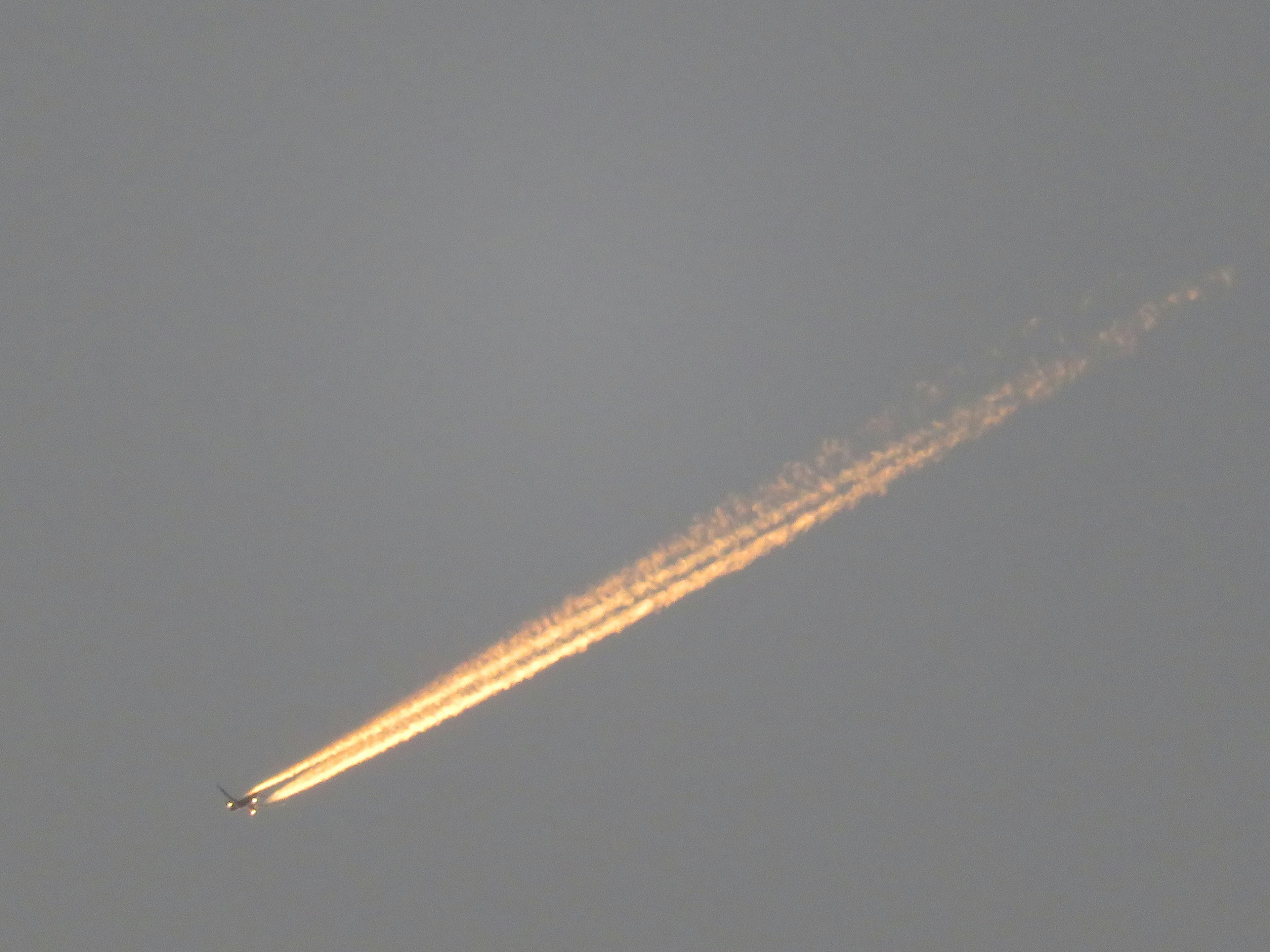 Flugzeug fliegt am Himmel und hinterlässt eine orangefarbene Kondensstreifen