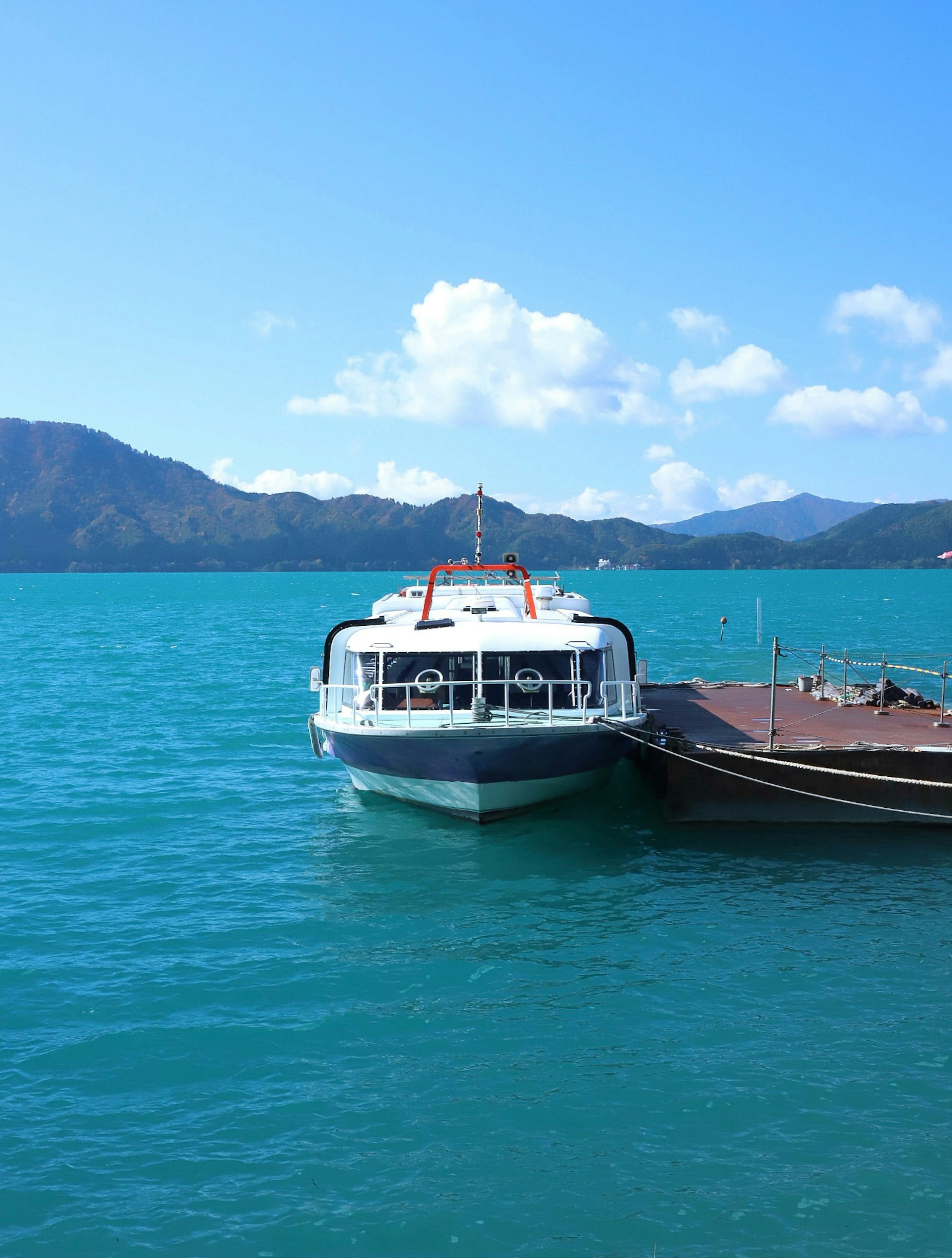 White boat docked in turquoise water with mountains in the background