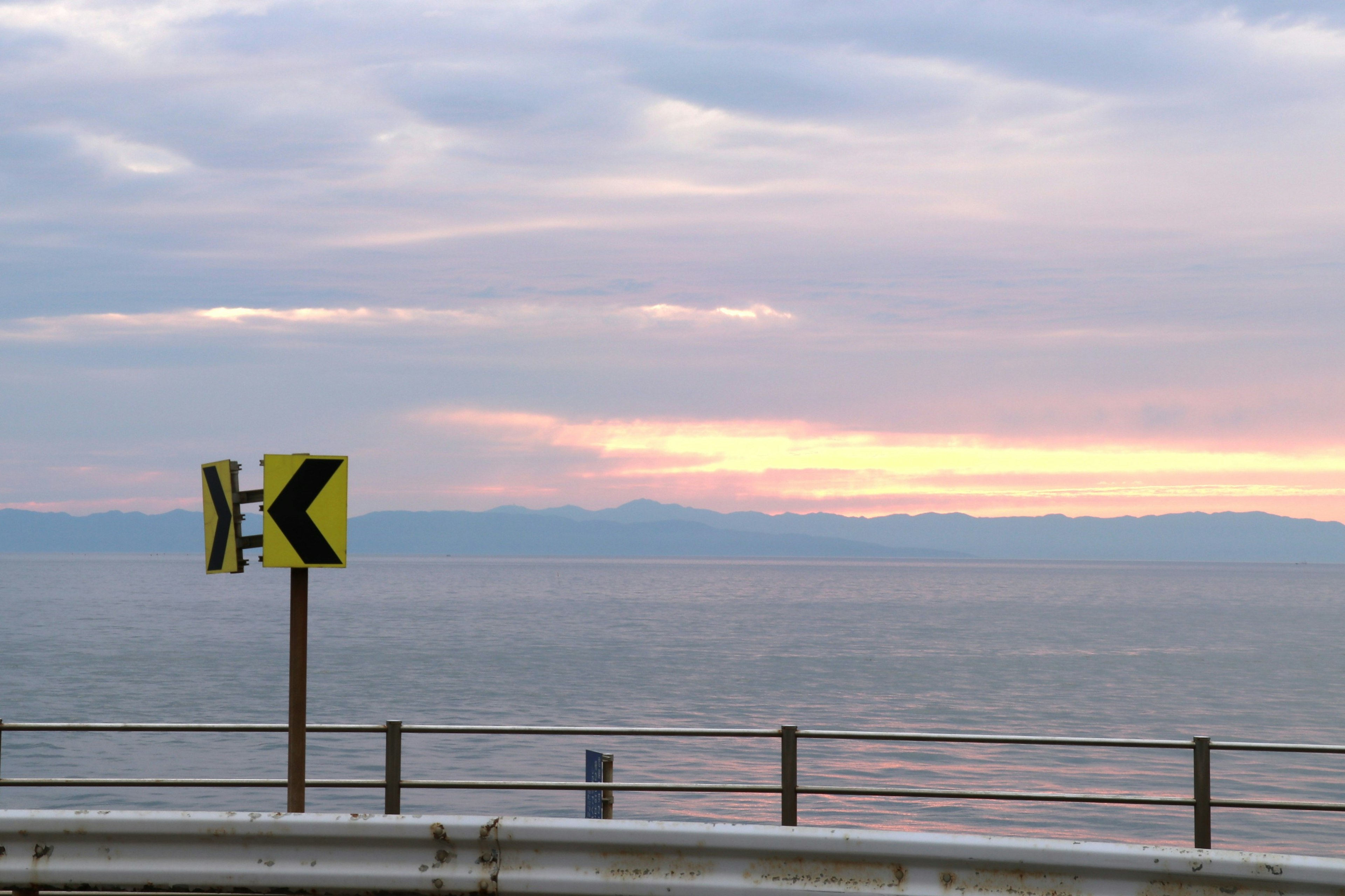 海岸線と夕焼けの背景に曲がりくねった道の標識